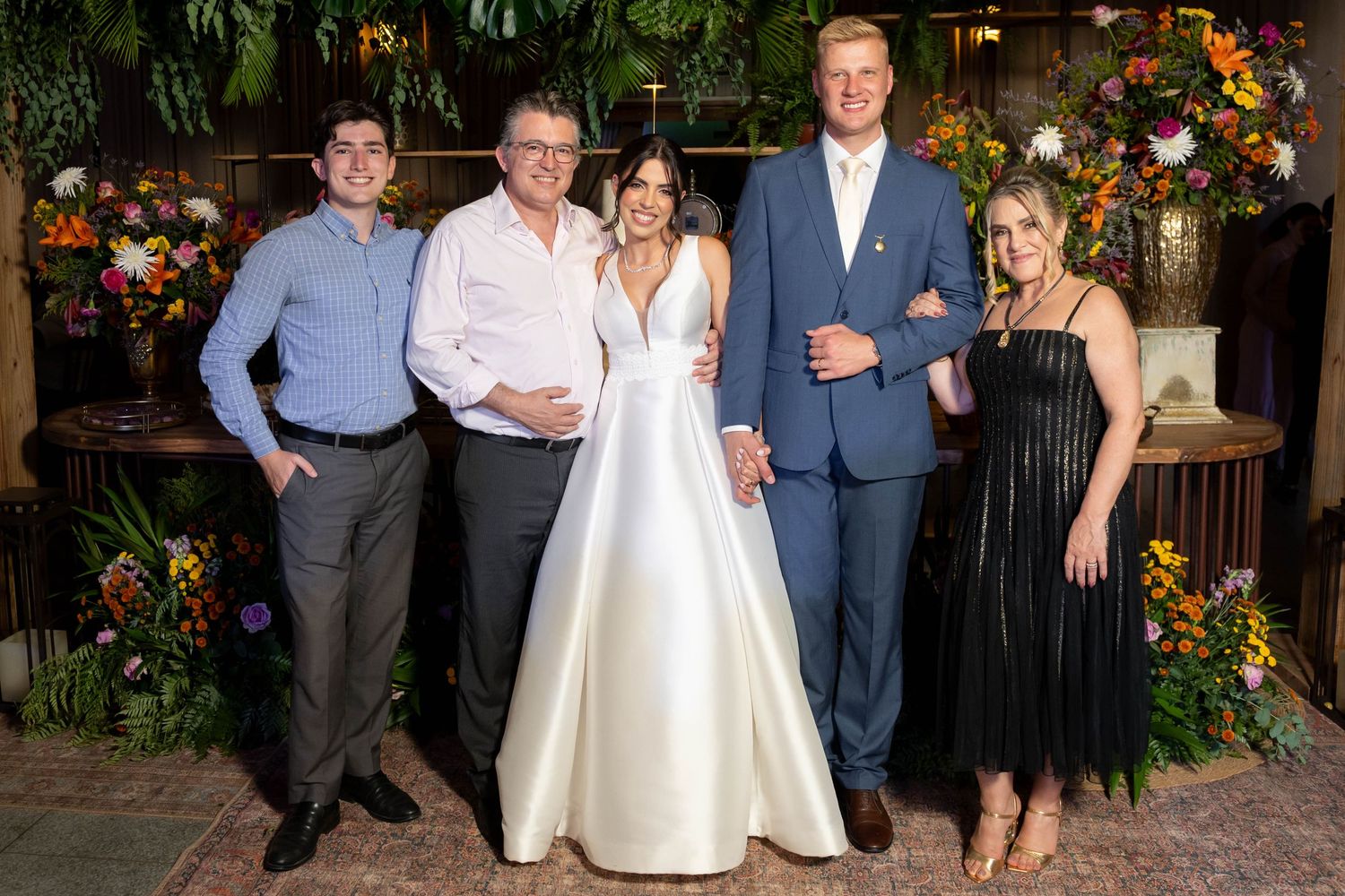 A bride in a white gown poses with four guests at a floral-decorated wedding reception venue.