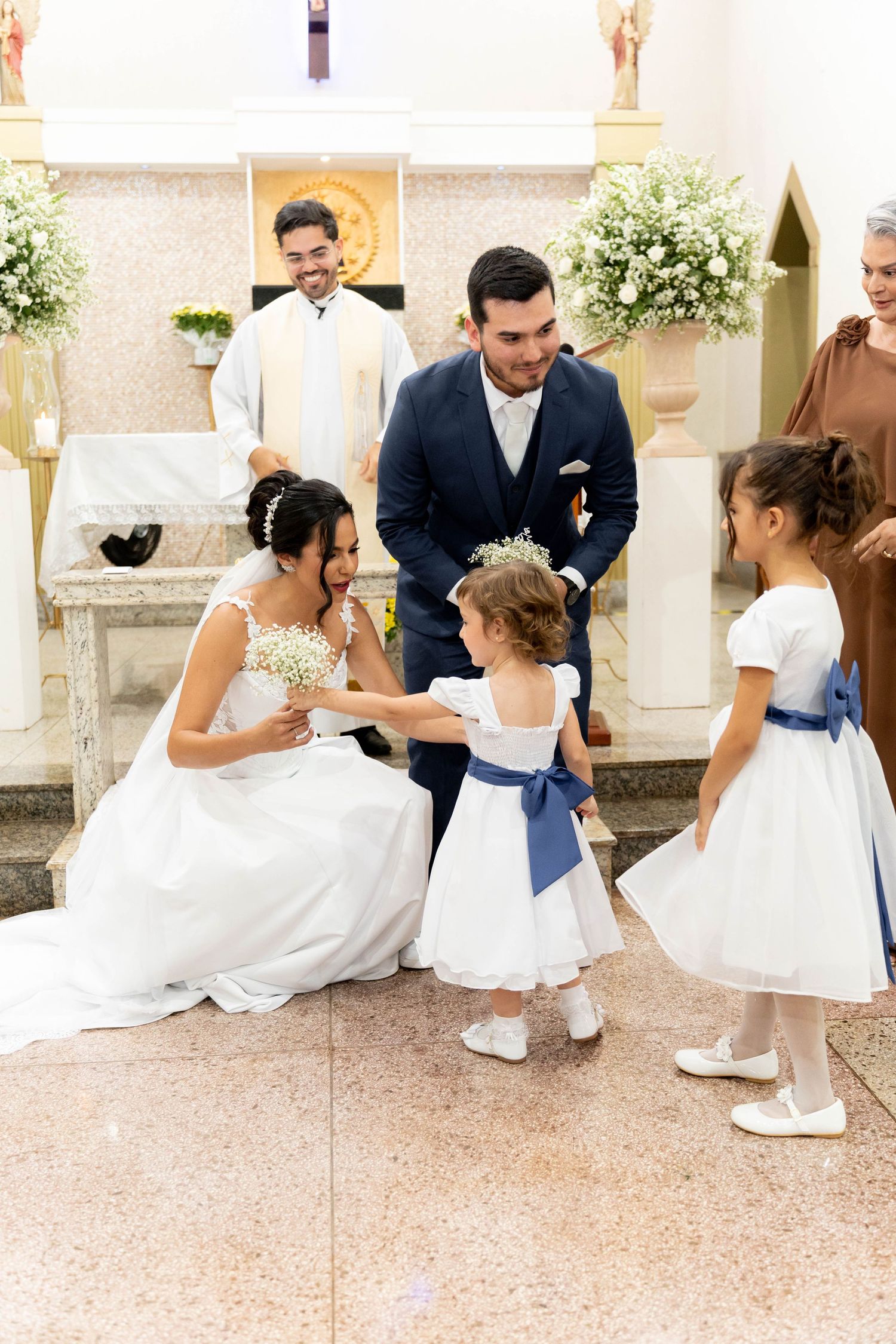 Bride and groom interact with flower girls in white dresses during a church wedding ceremony.