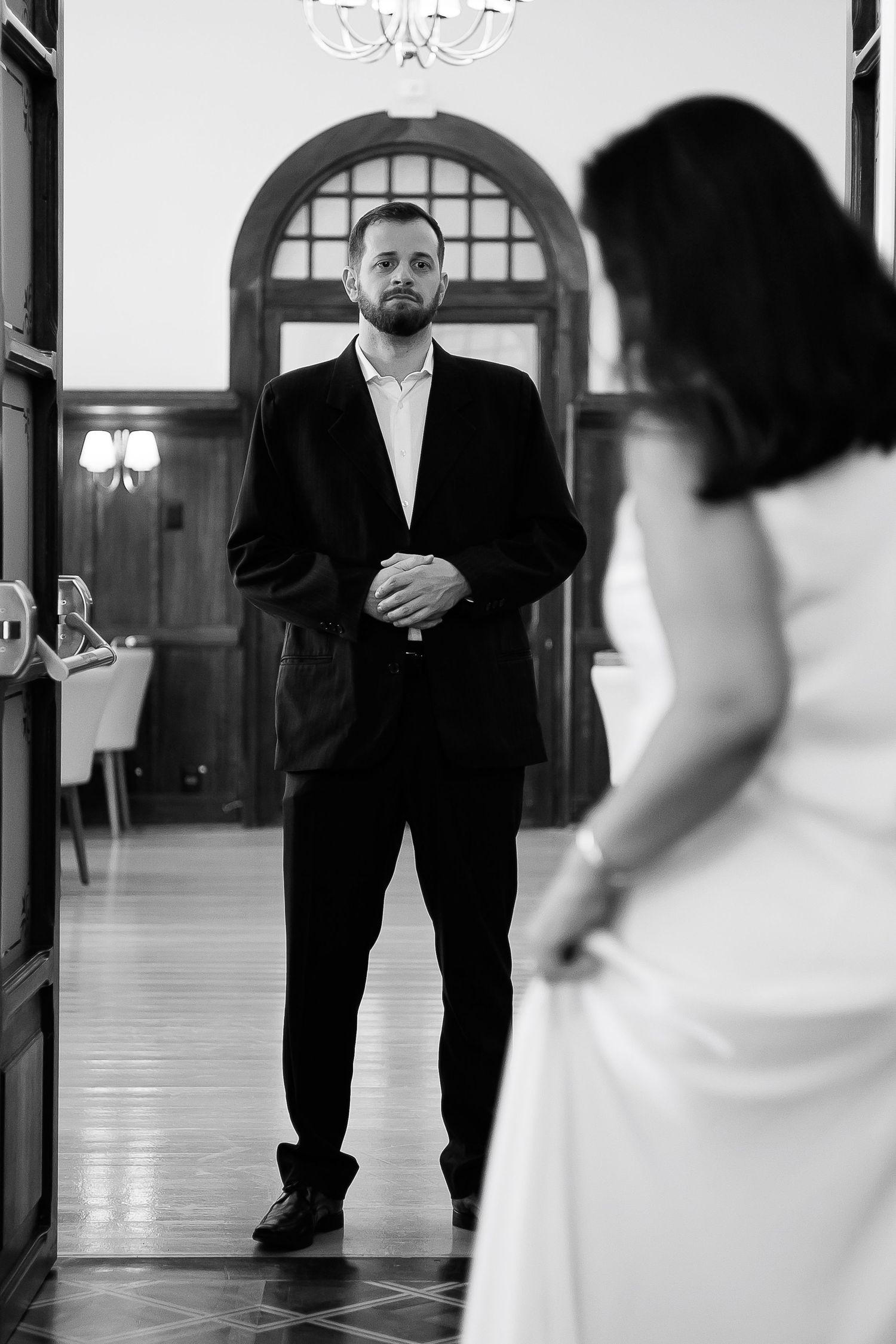 Black and white photo of a groom in a suit gazing at a bride in a white dress in an elegant hall.