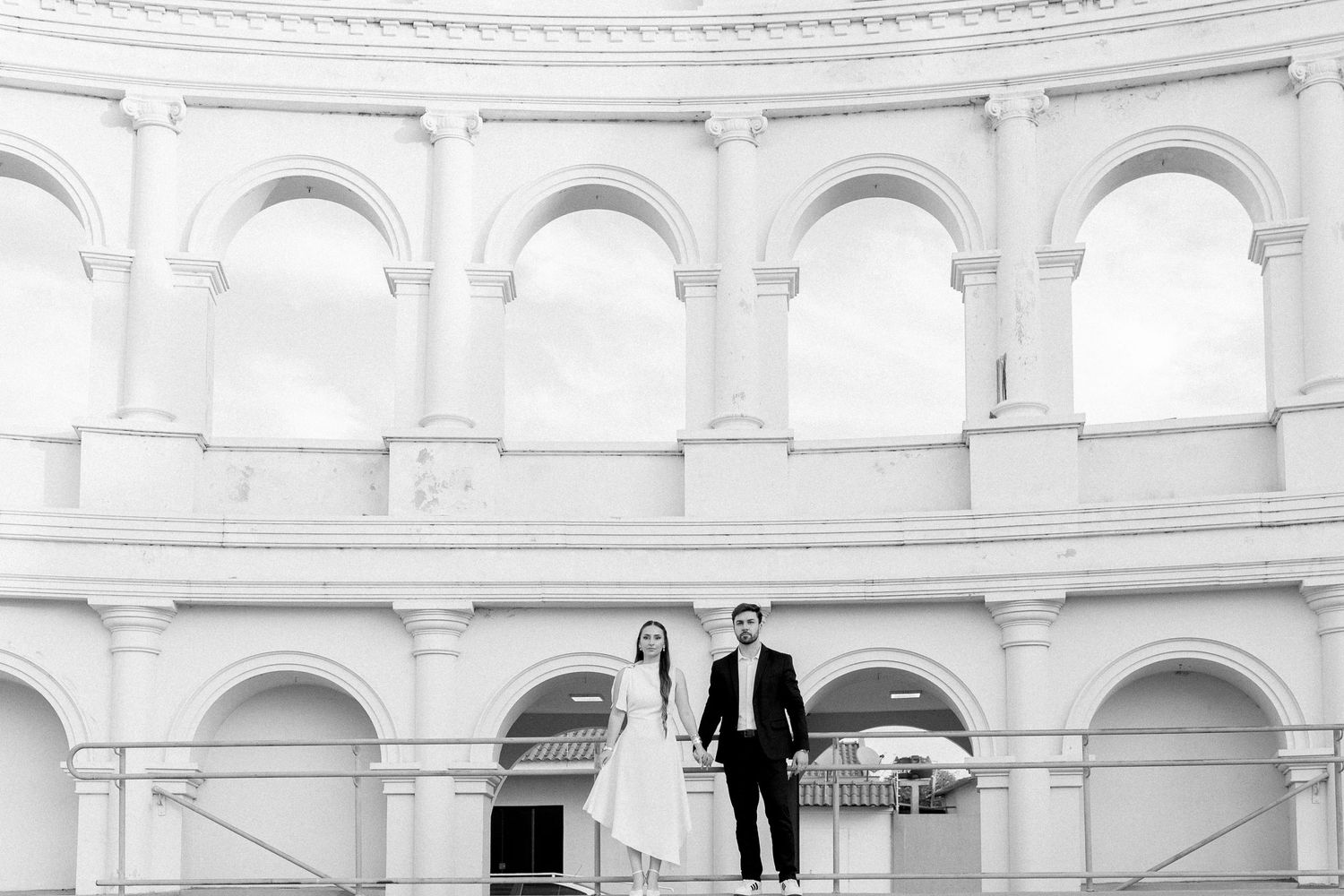 Couple poses elegantly in black and white photo at a grand neoclassical rotunda with arched columns.