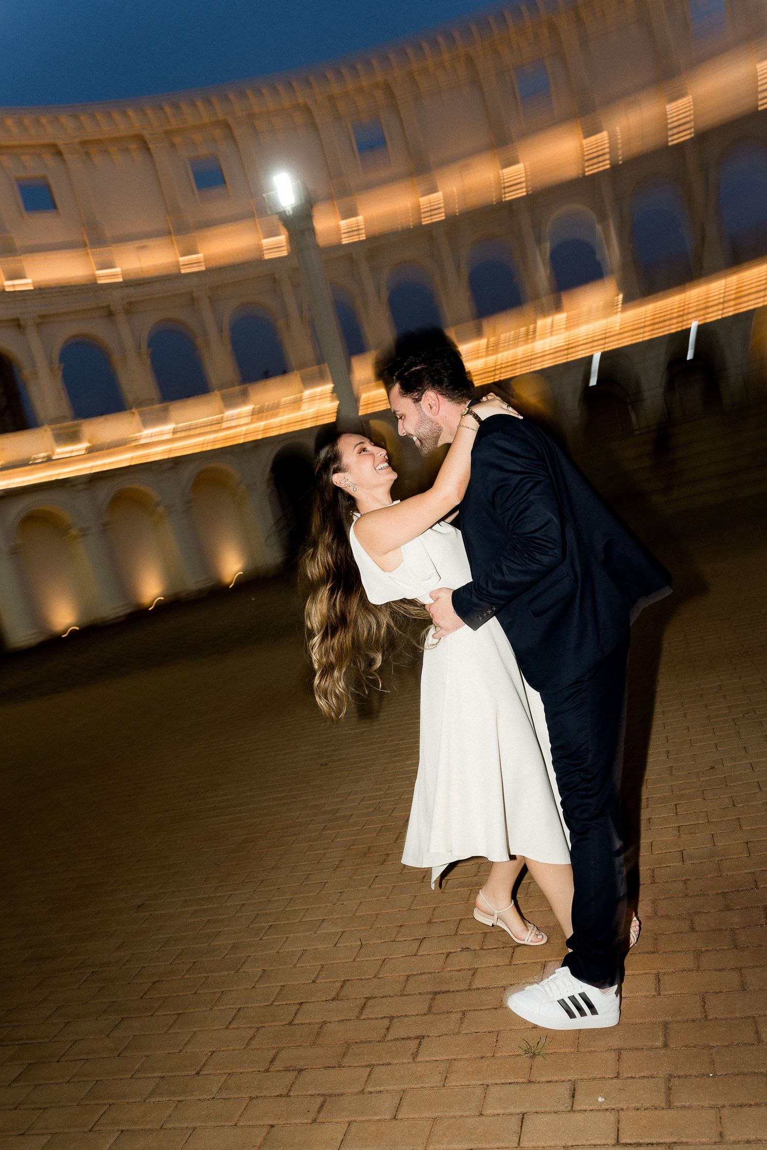 Couple sharing a romantic dance at night in front of the illuminated Colosseum in Rome, Italy.