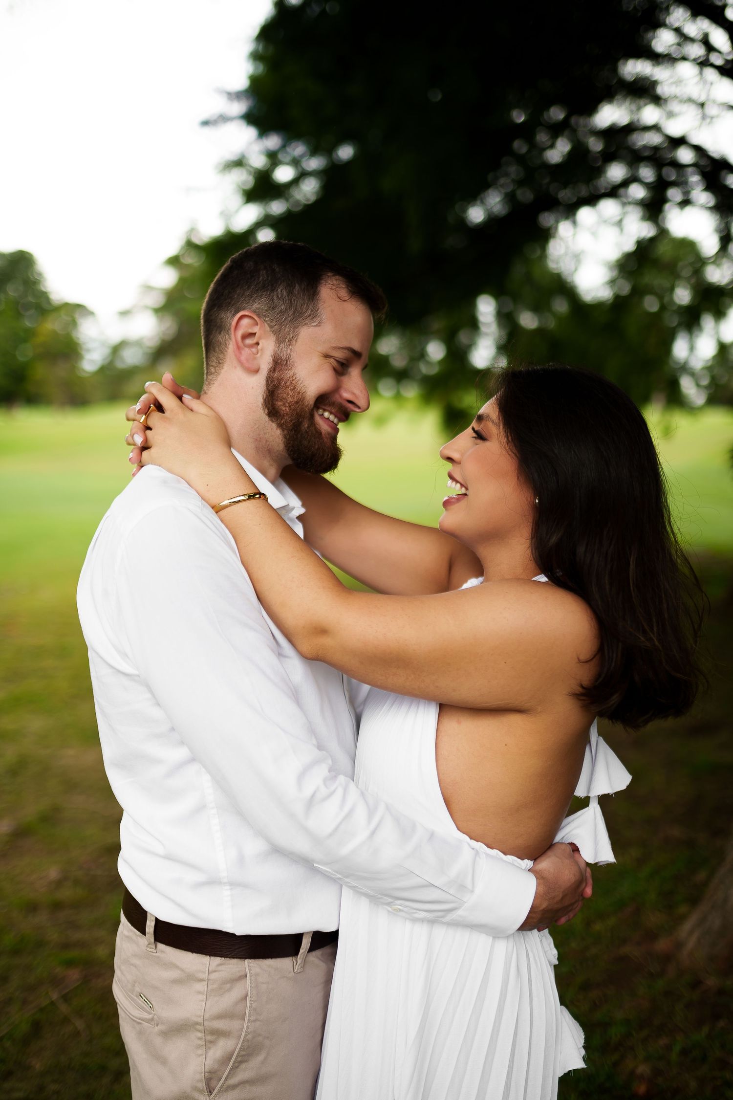 Happy couple in white embracing and smiling outdoors in a lush green park setting.