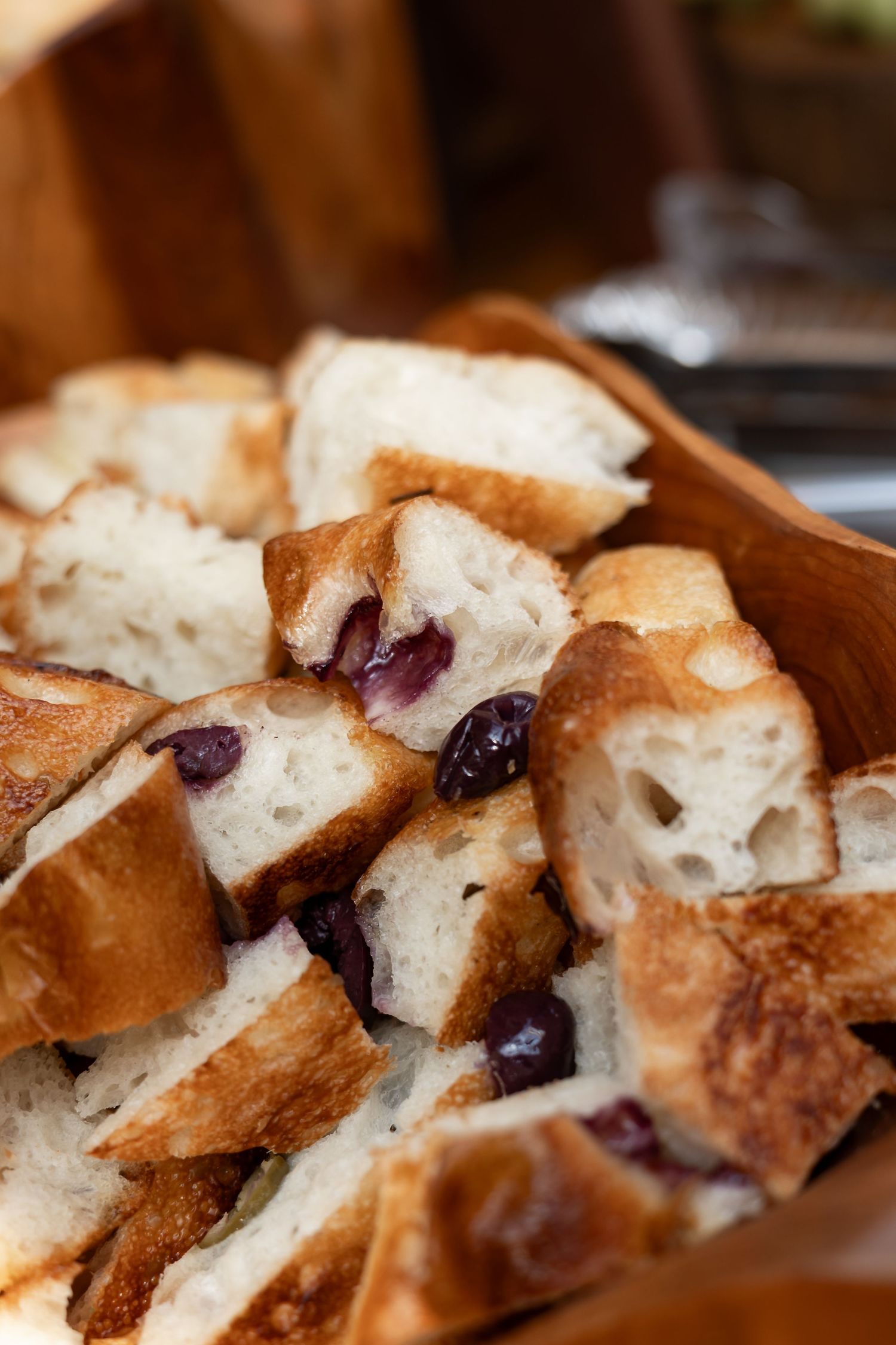 Chunks of rustic olive bread with golden crust served in a wooden bowl.