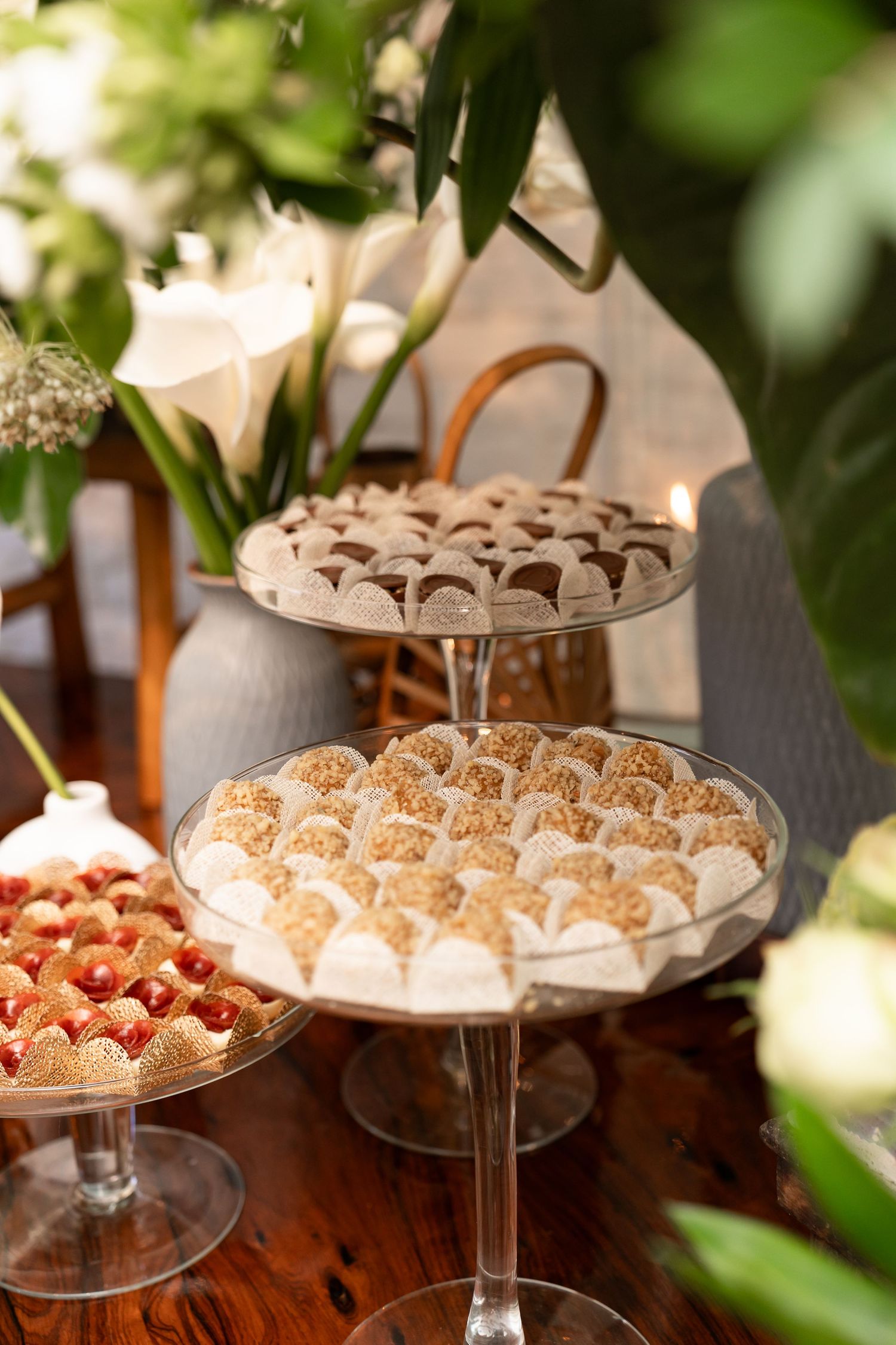 Elegant two-tiered dessert stand with assorted sweets beside fresh strawberries and white floral arrangements on a wooden table.