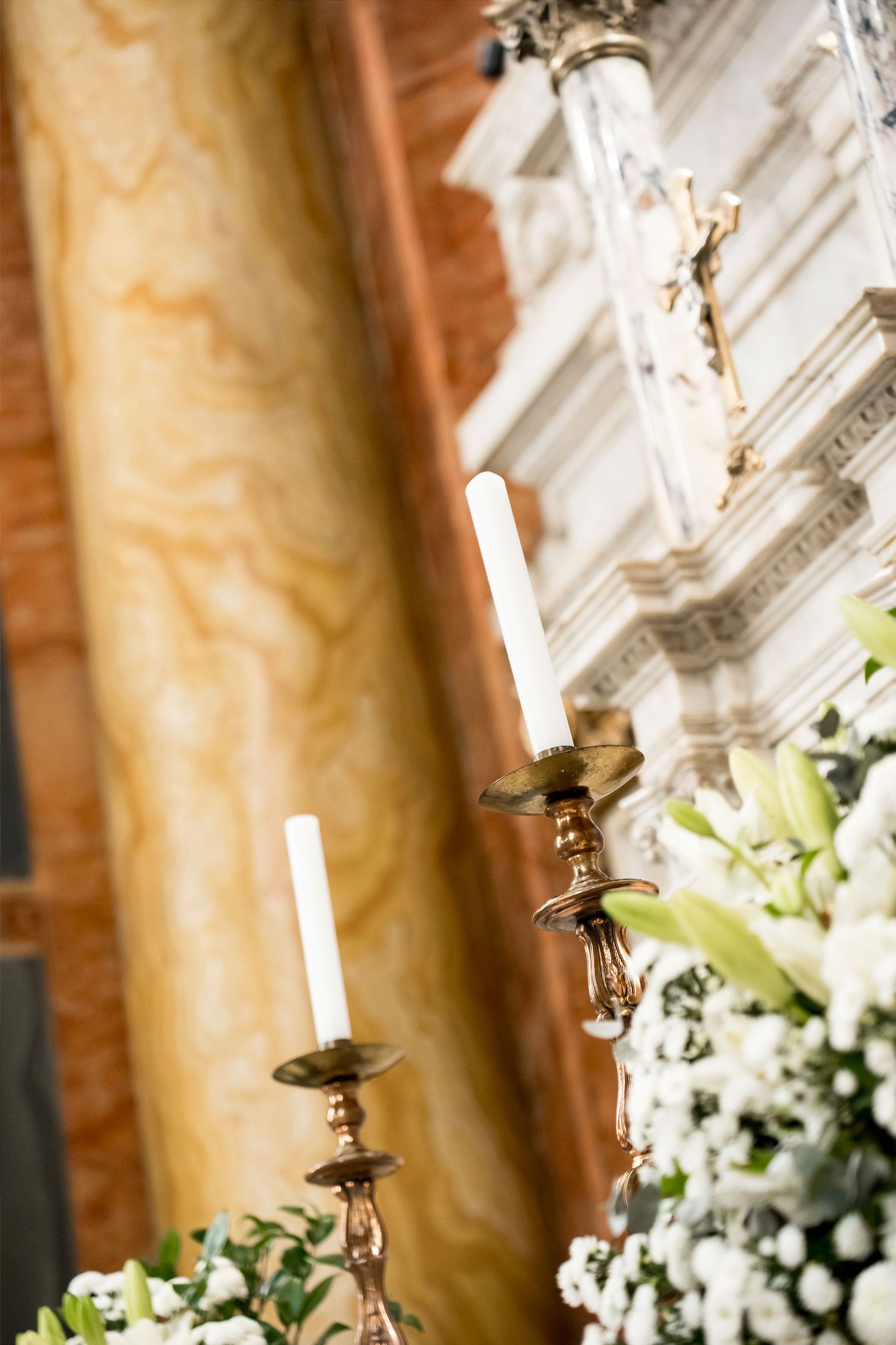 Gold candelabras with white candles adorn a church altar surrounded by white lilies and floral arrangements.
