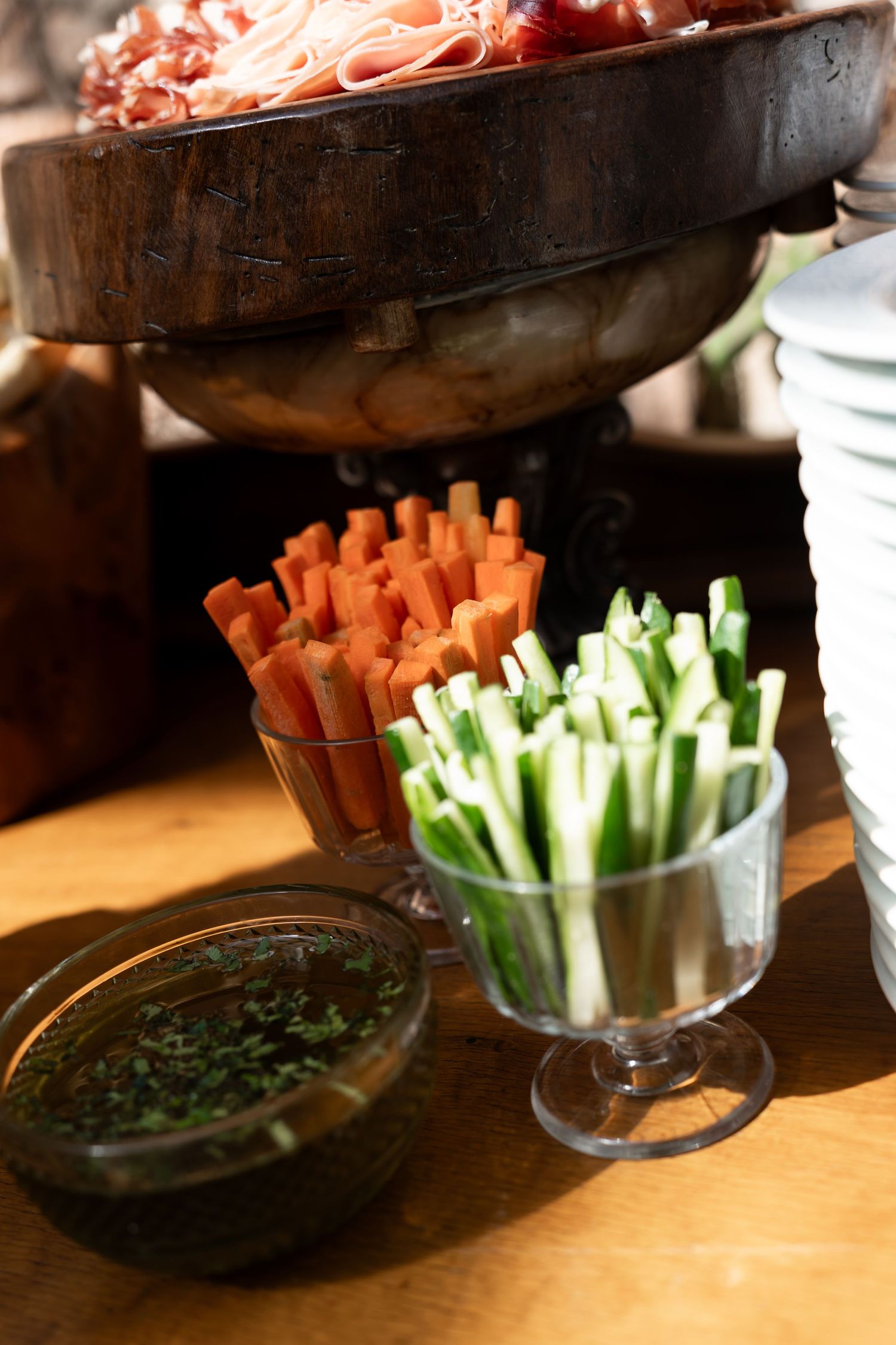 Fresh carrot and cucumber sticks in glass cups served with herb dipping sauce on a wooden table.