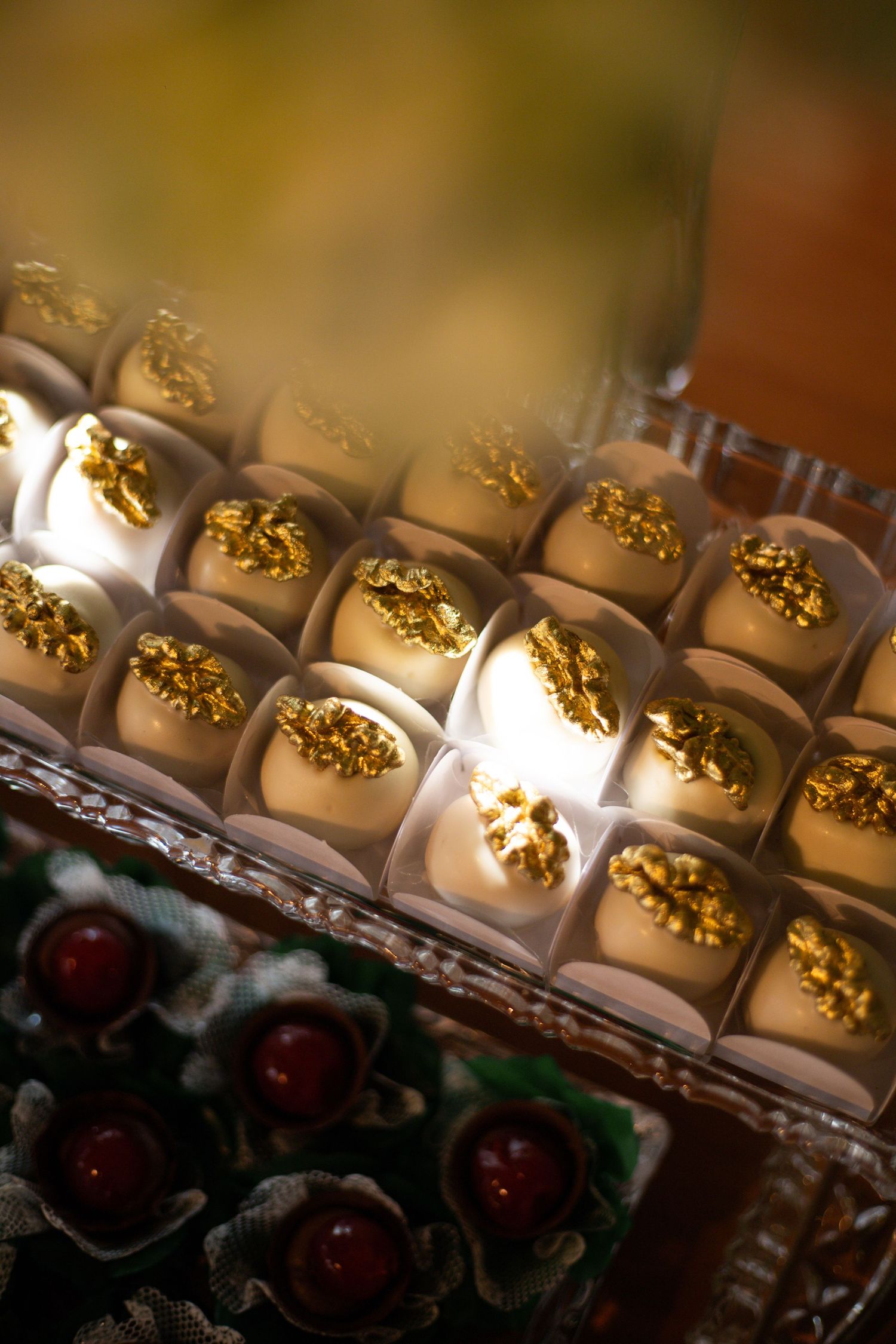 Elegant white chocolate truffles topped with edible gold leaf arranged in a display box at a luxury event.