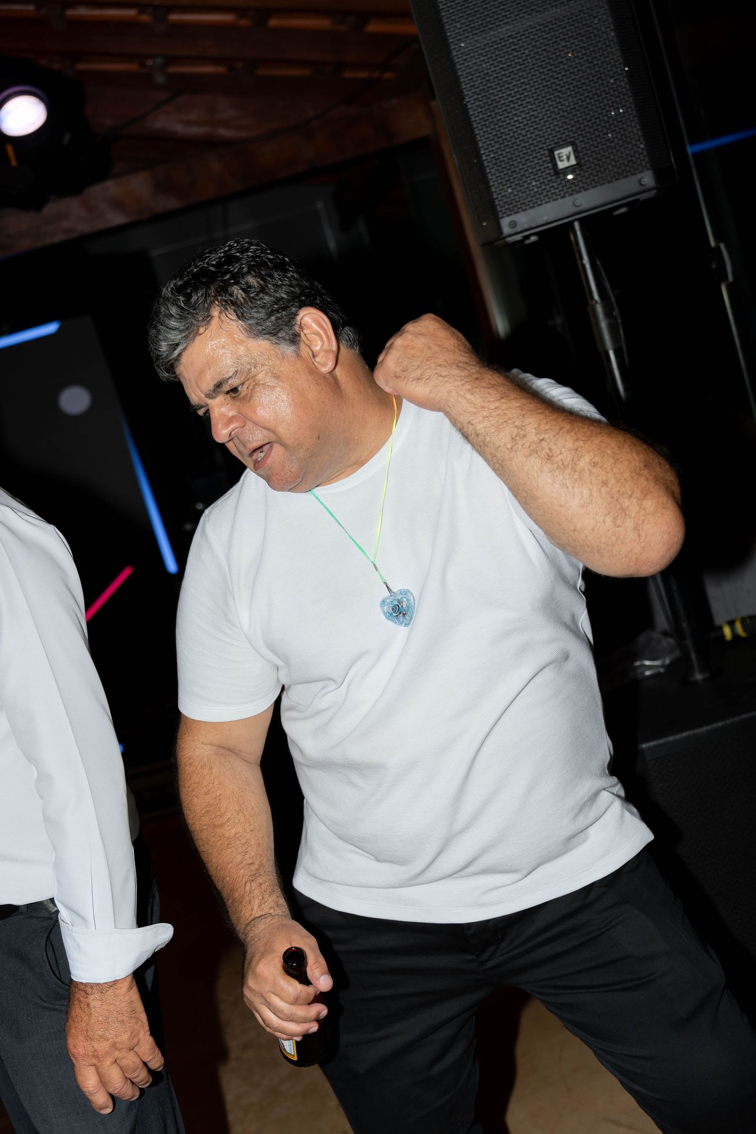 Man in white t-shirt dancing energetically at a party event with speakers in background.