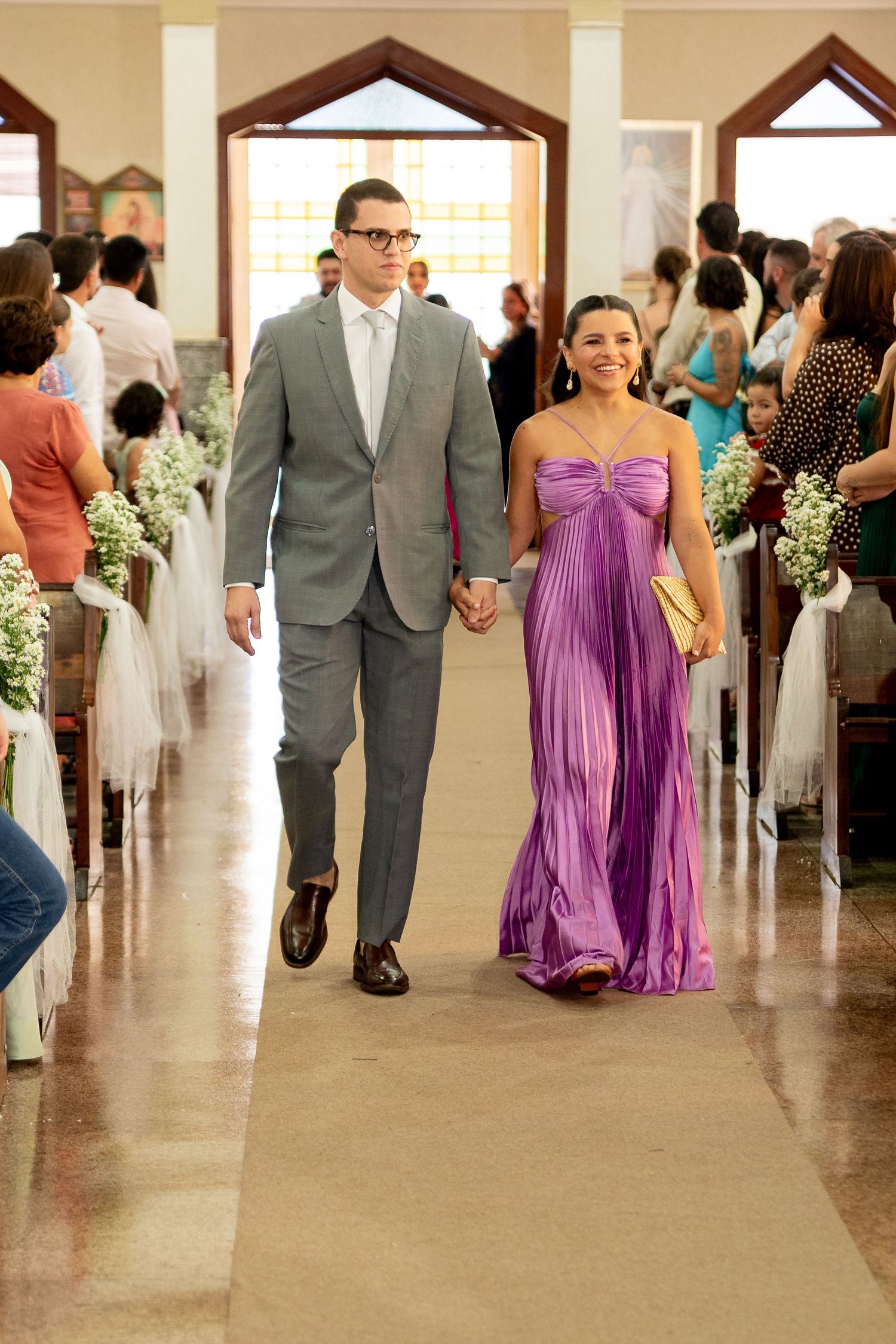 A couple walks down a church aisle, man in gray suit, woman in purple gown, at a wedding ceremony.