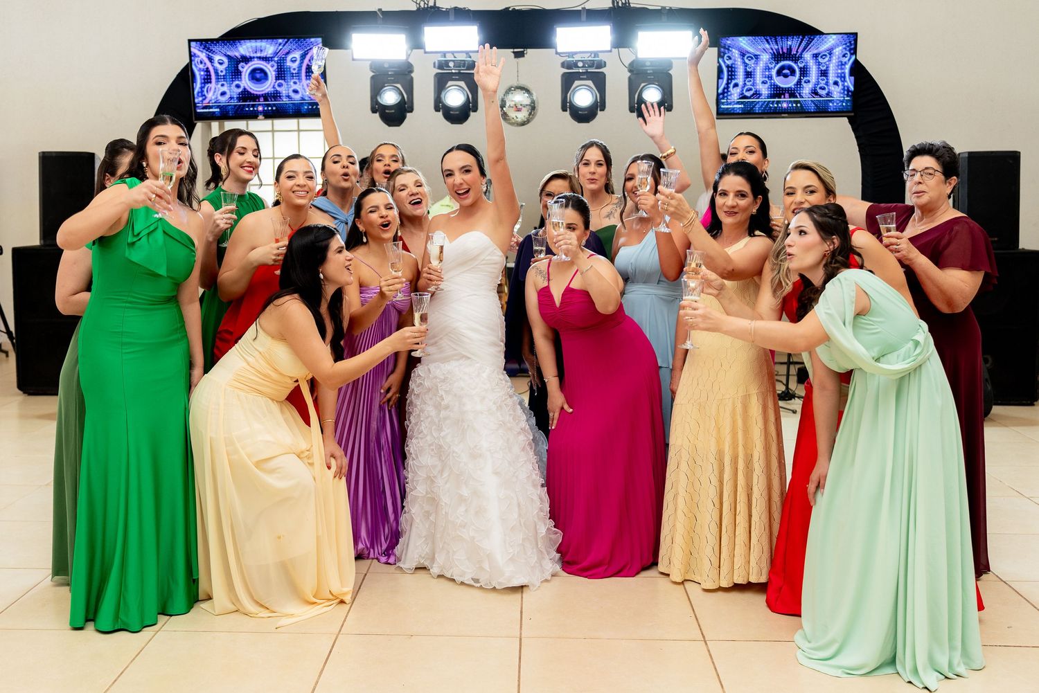 Bride in white gown celebrates with bridesmaids in colorful dresses at a wedding reception venue.