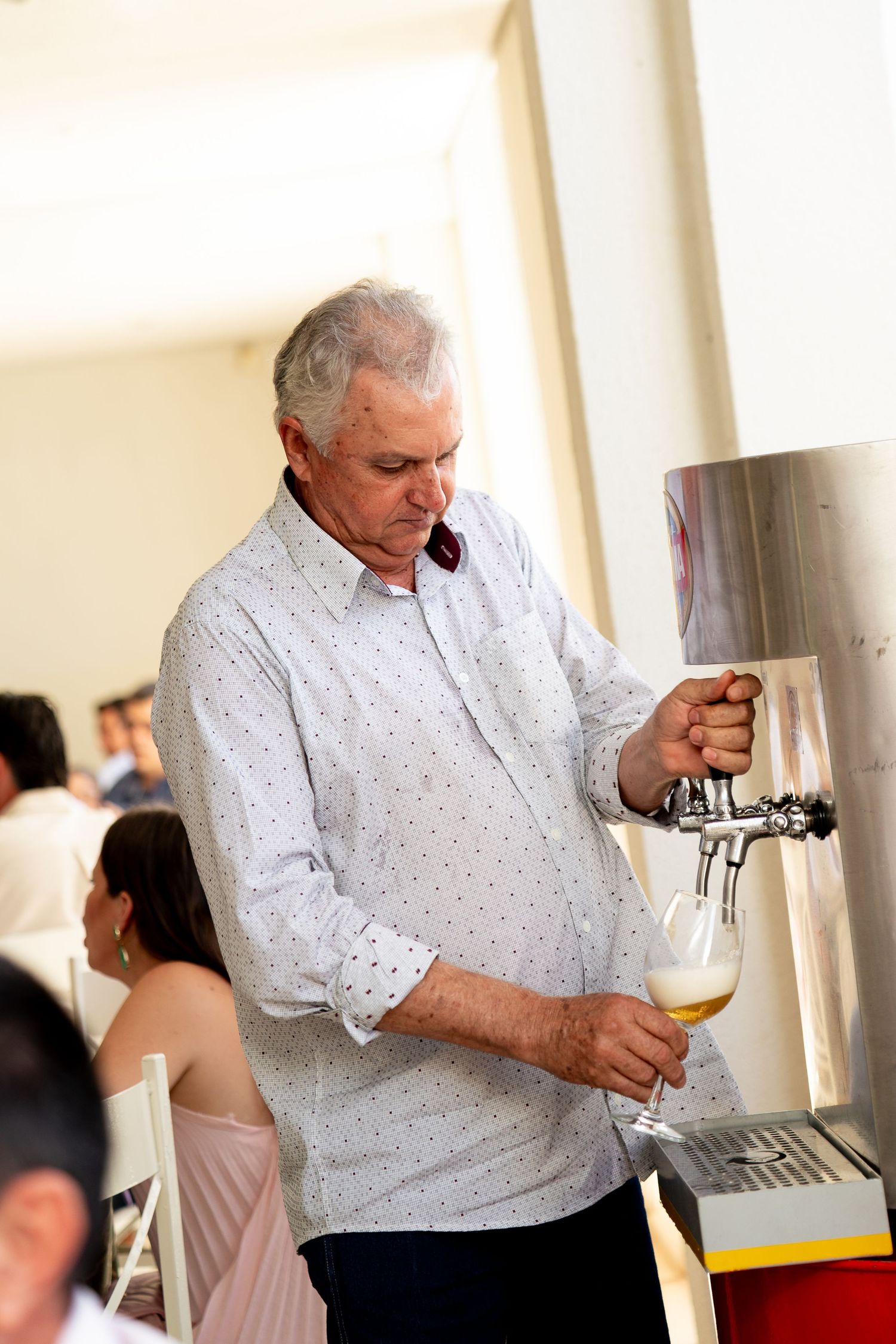 Elderly man pouring draft beer from a tap dispenser into a glass at an outdoor event.
