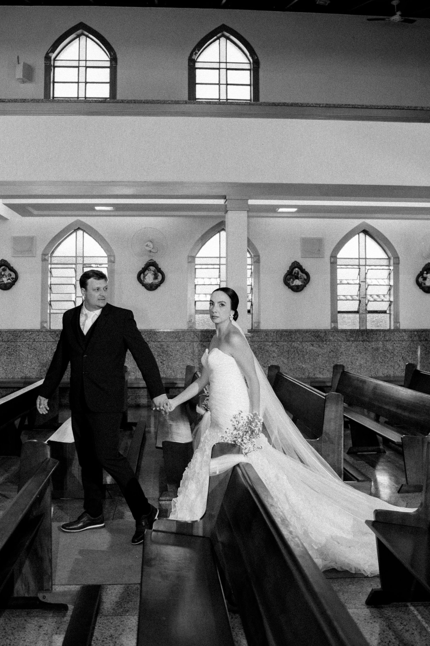 Black and white photo of a bride and groom holding hands walking down the aisle of a church after their wedding ceremony.