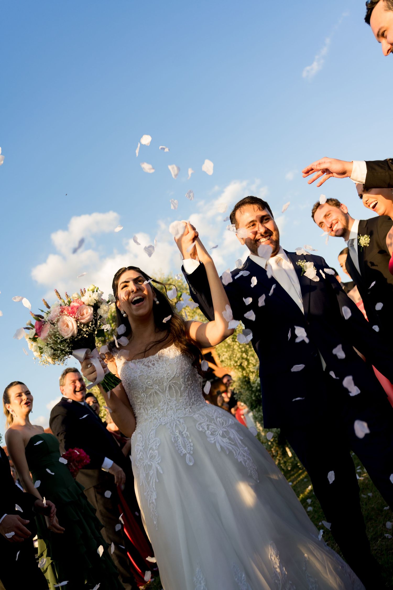 Joyful newlyweds walk down the aisle as guests toss white flower petals in celebration.