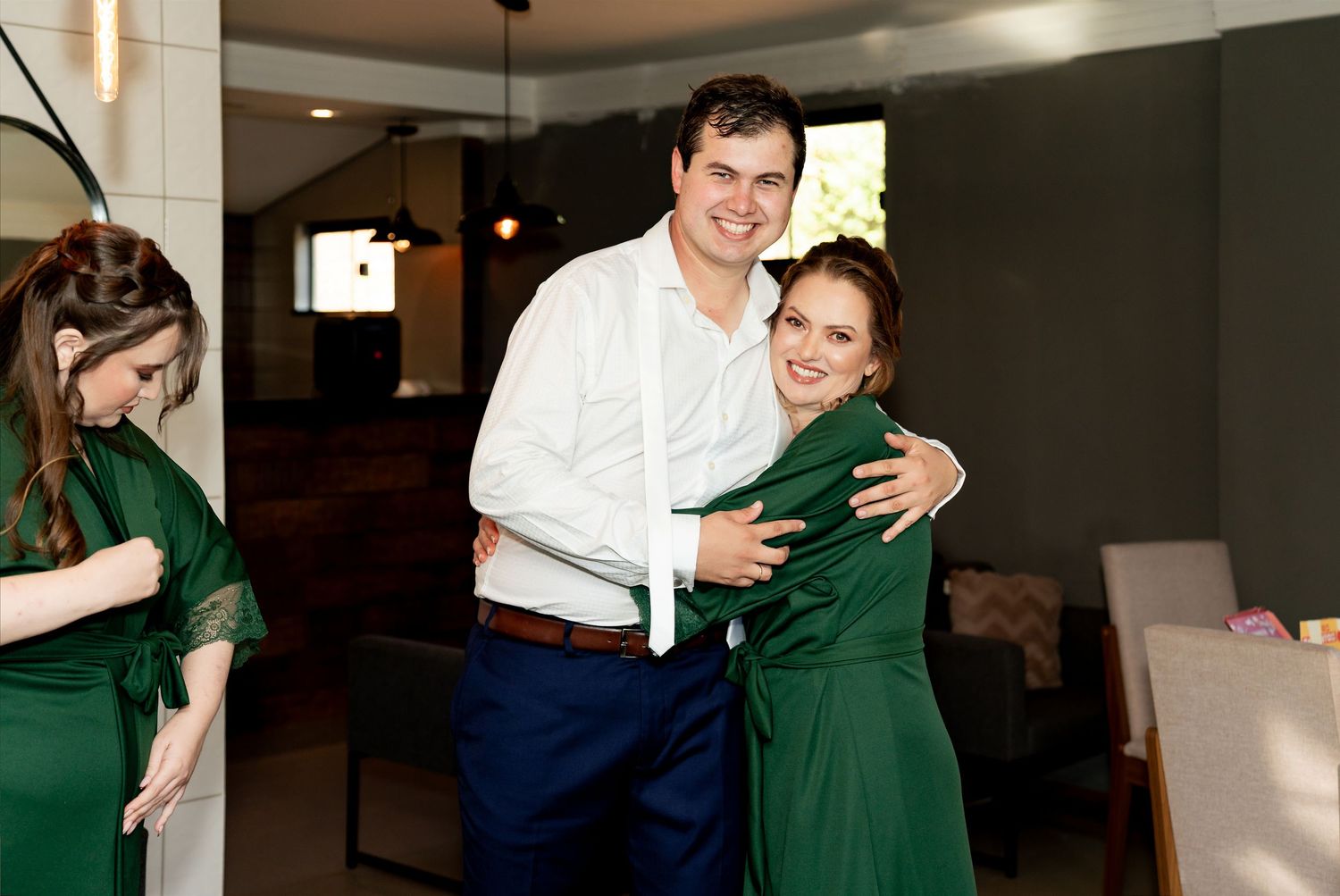 Man and woman in green dress sharing a warm hug at an indoor event, with another woman in green nearby.