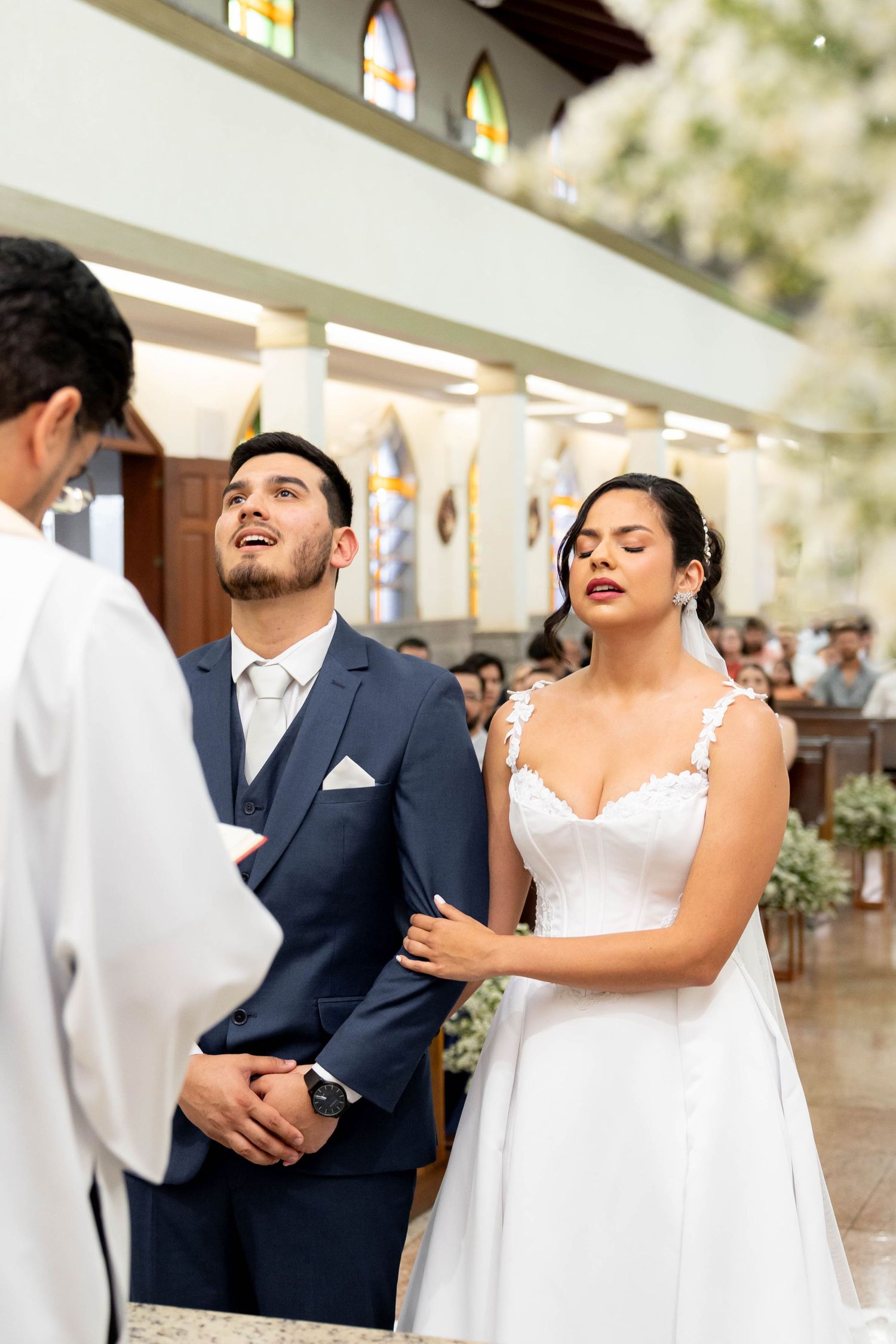 Bride and groom exchanging vows at a church wedding ceremony, bride in white lace gown, groom in navy suit.
