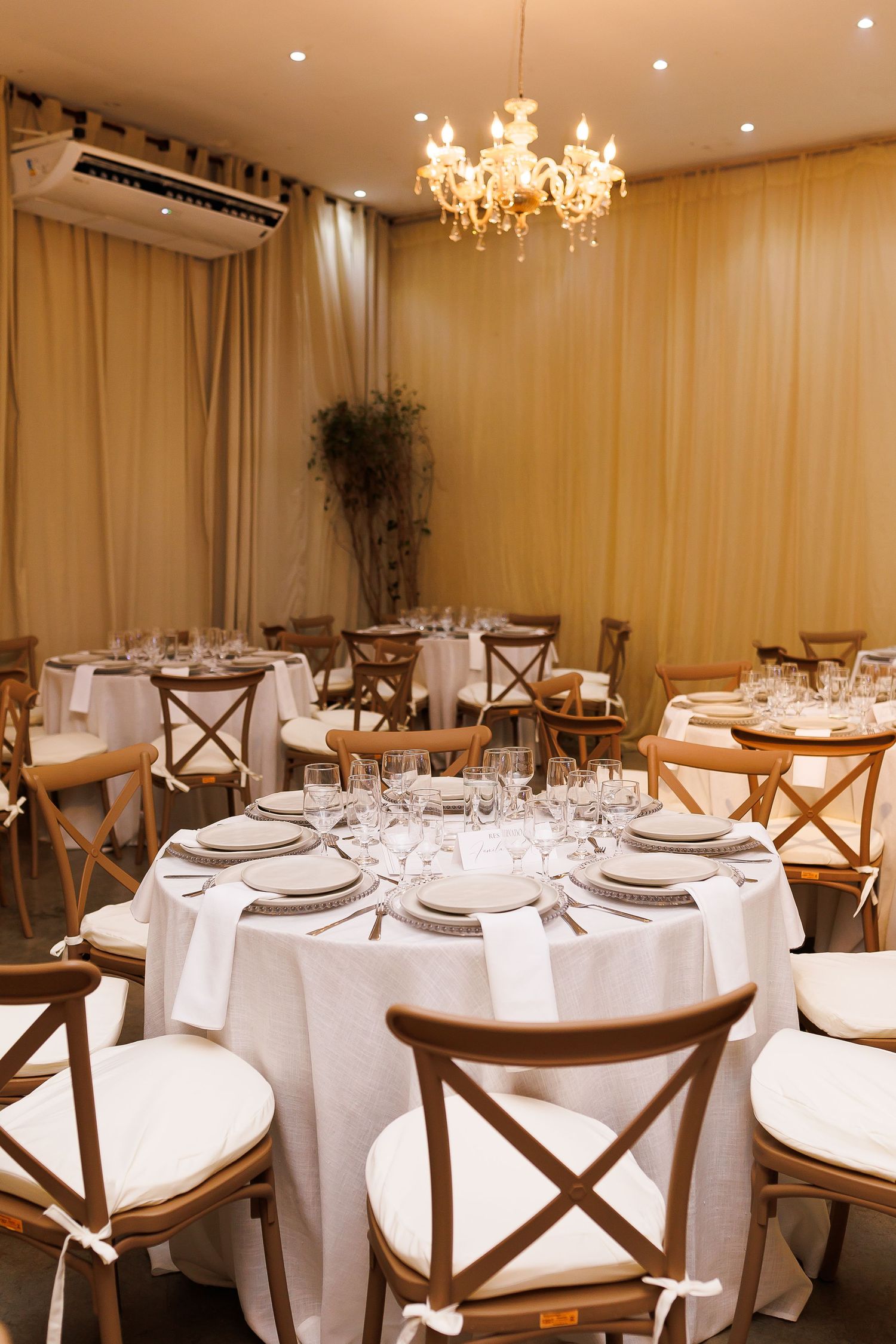 Elegant banquet hall with round tables, white linens, cross-back chairs, and a chandelier for weddings or events.