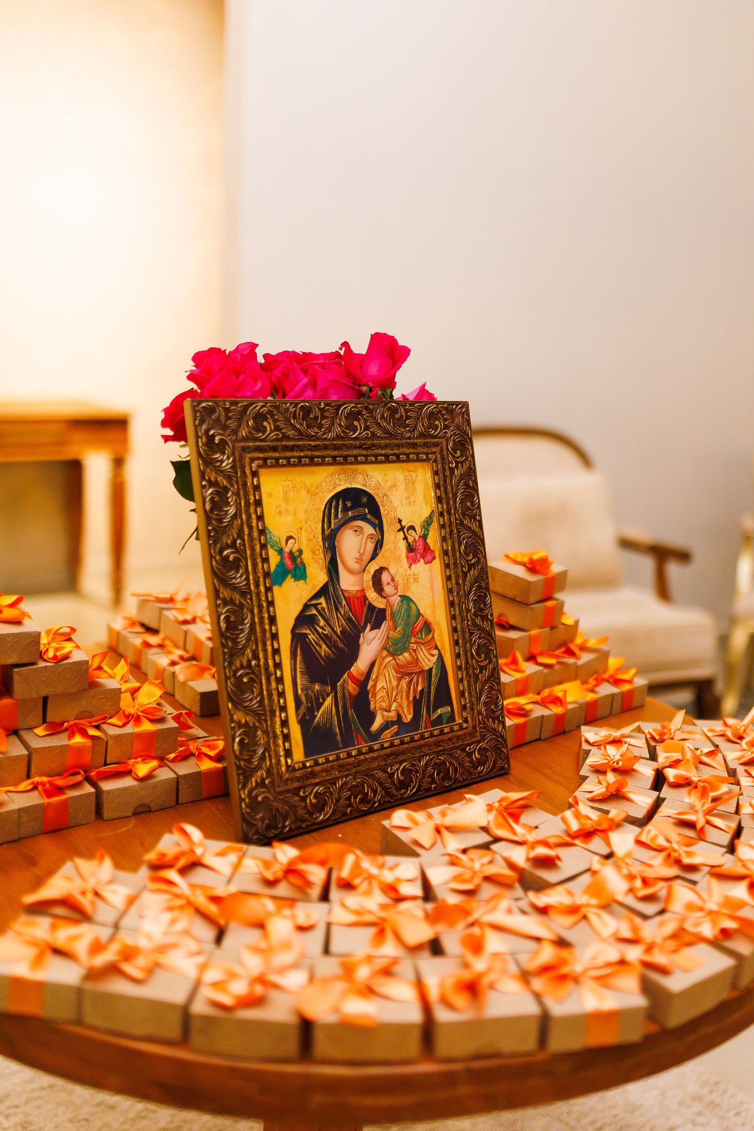 Orthodox icon of Virgin Mary with Christ child, surrounded by small gift boxes with orange bows on a wooden table.