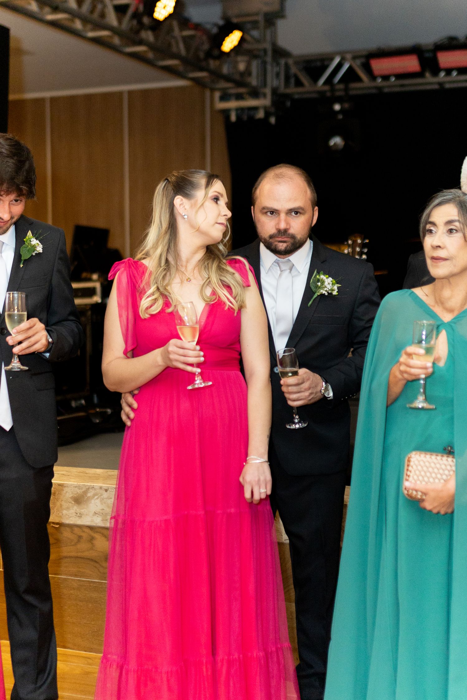 Elegantly dressed guests at a formal event, woman in pink gown holding champagne, man in black suit beside her.