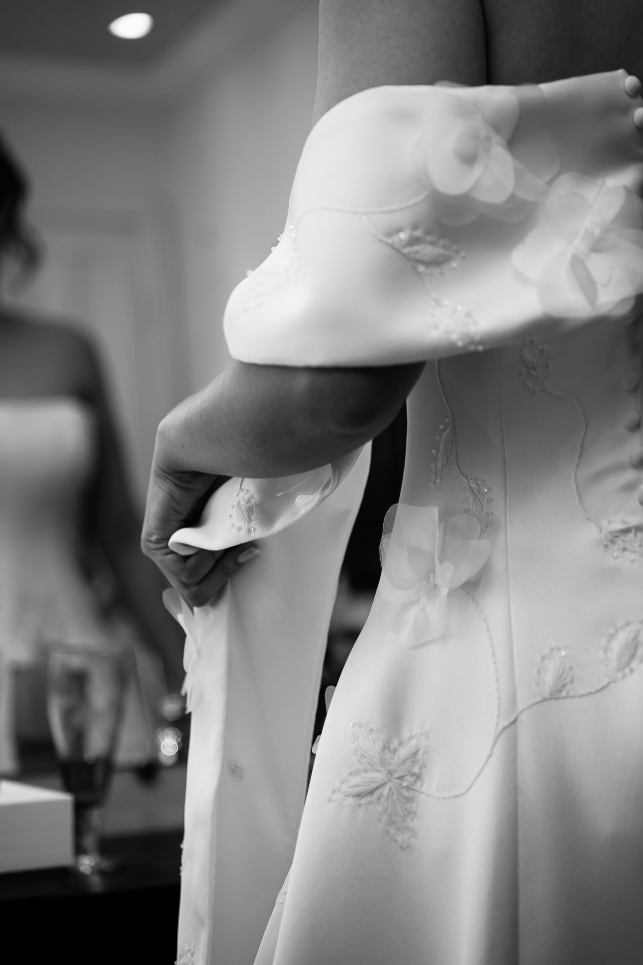 Close-up black and white photo of hands fastening buttons on a bridal wedding gown.