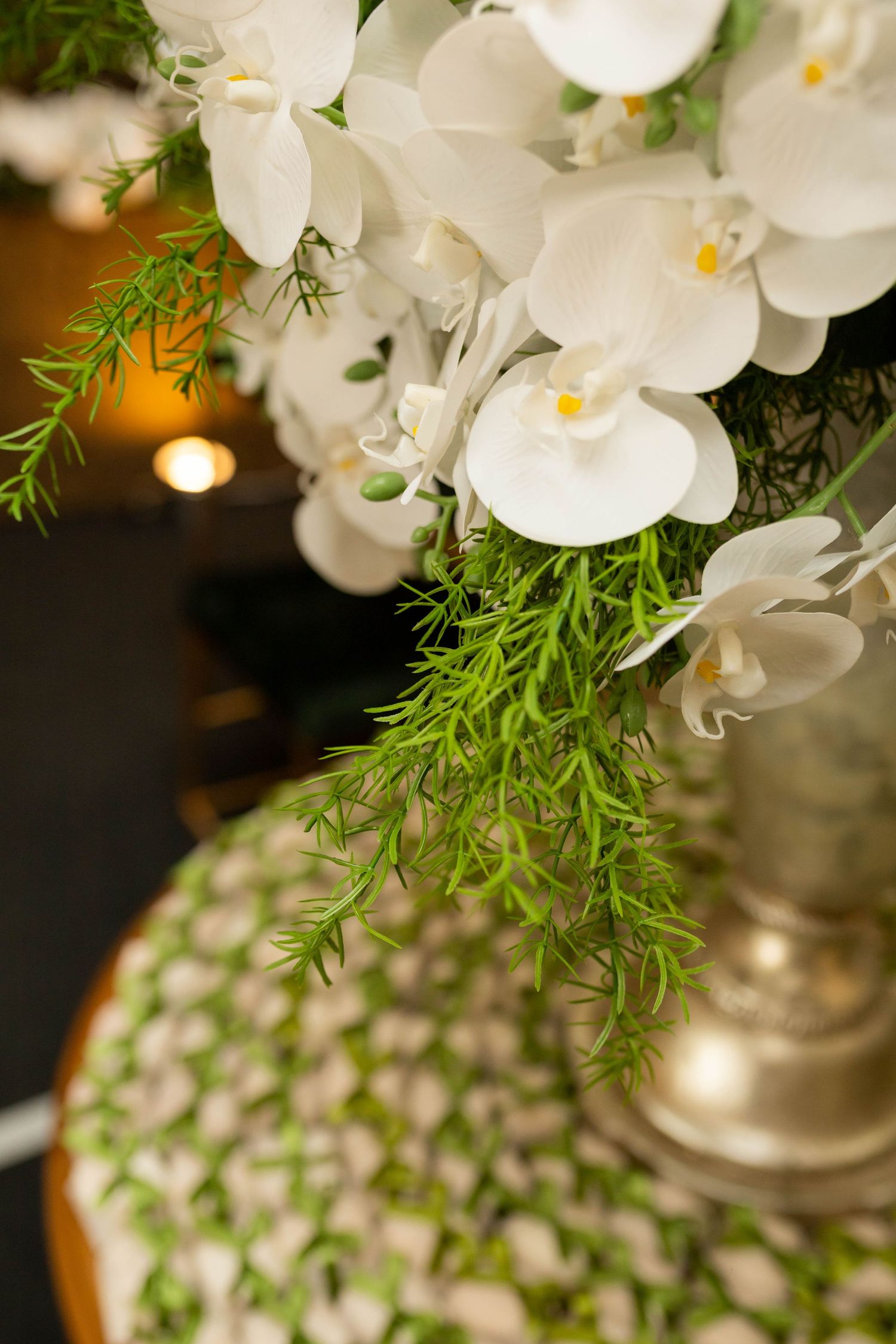 Elegant white orchid arrangement with lush green ferns in a silver vase, perfect for wedding or event decor.