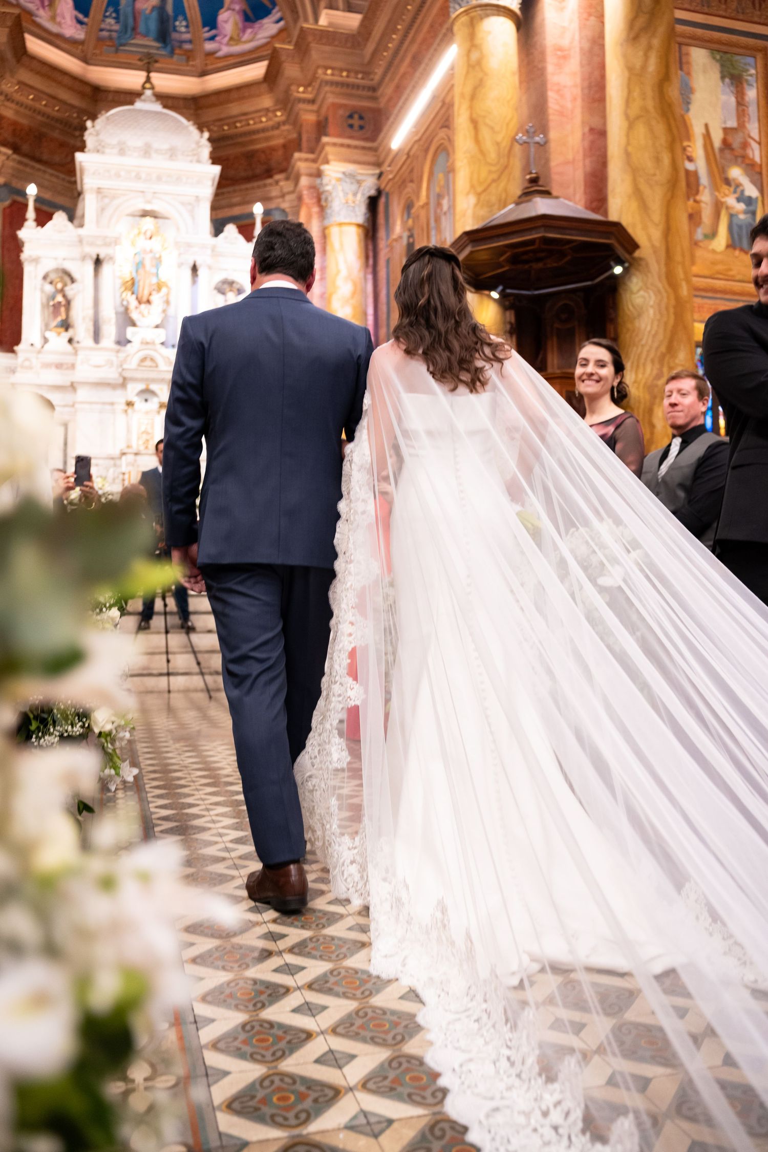 Bride and groom walking down the aisle of an ornate church, bride wearing a long lace veil.