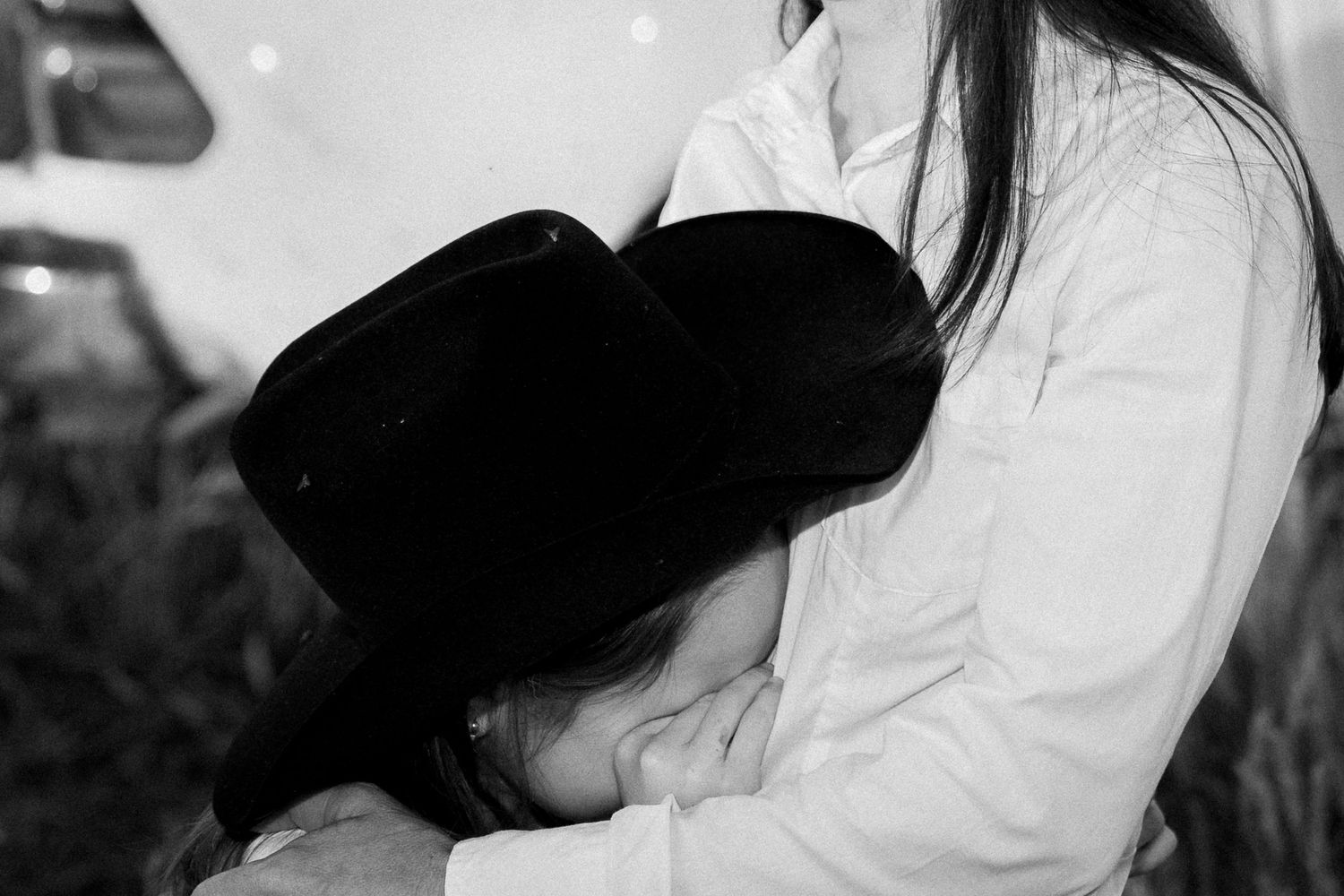Black and white photo of a woman in white shirt embracing a person wearing a black cowboy hat.