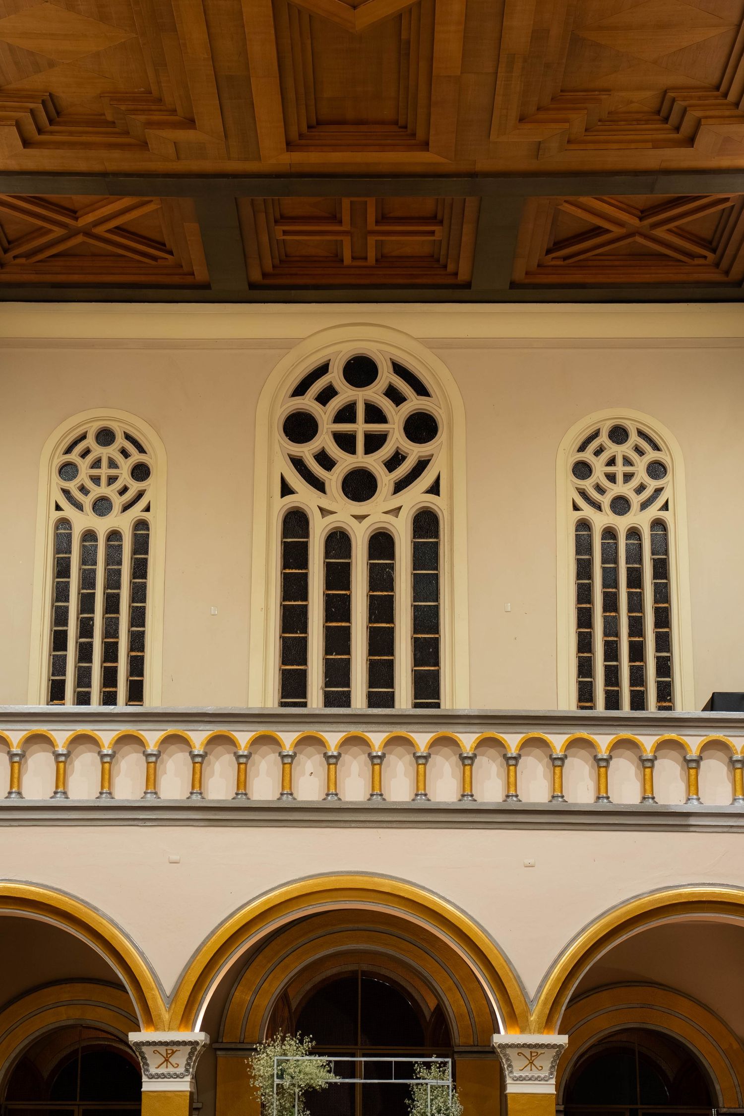 Ornate church facade with arched Gothic windows, decorative balustrade, yellow arched colonnade, and wooden coffered ceiling.