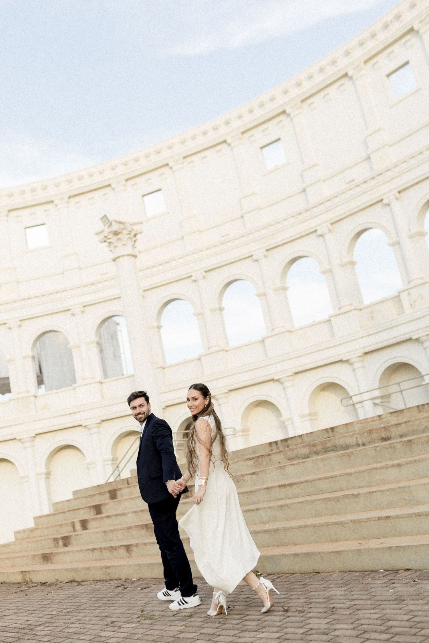 Couple in wedding attire holding hands in front of the Colosseum in Rome, Italy.
