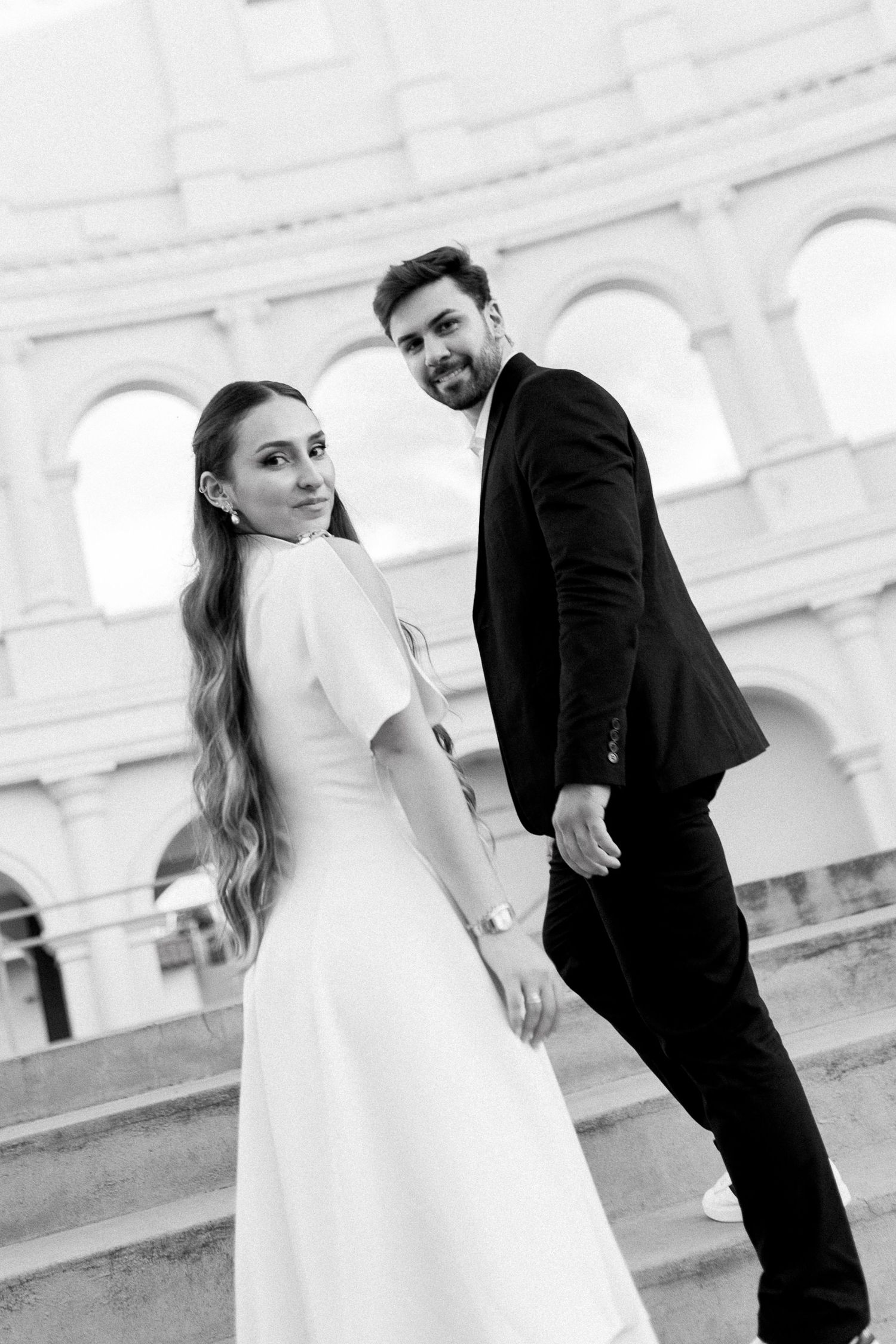 Black and white photo of a bride and groom holding hands on steps in front of the Colosseum in Rome.