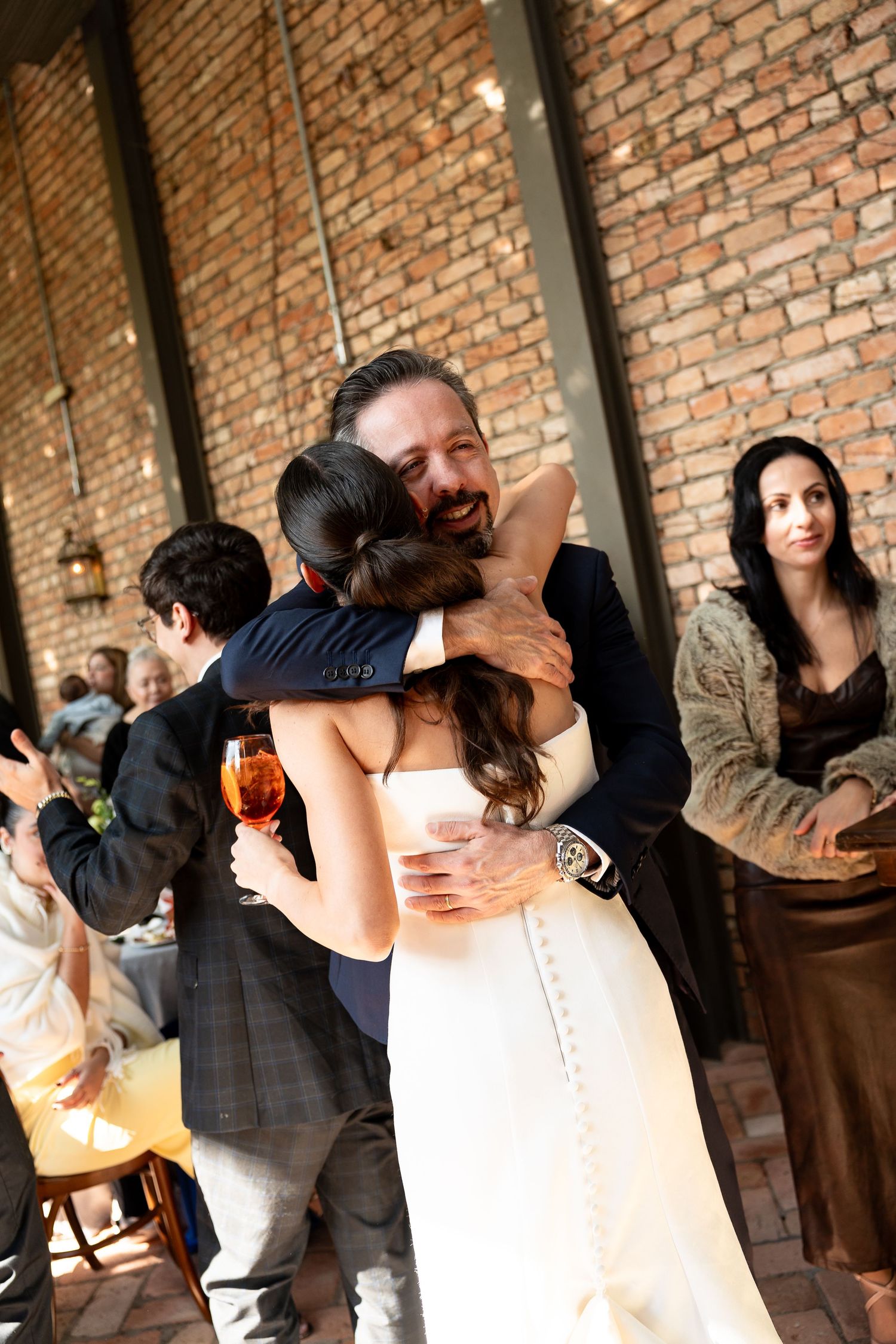 A bride and groom share a warm embrace at their wedding reception in a rustic brick-walled venue.