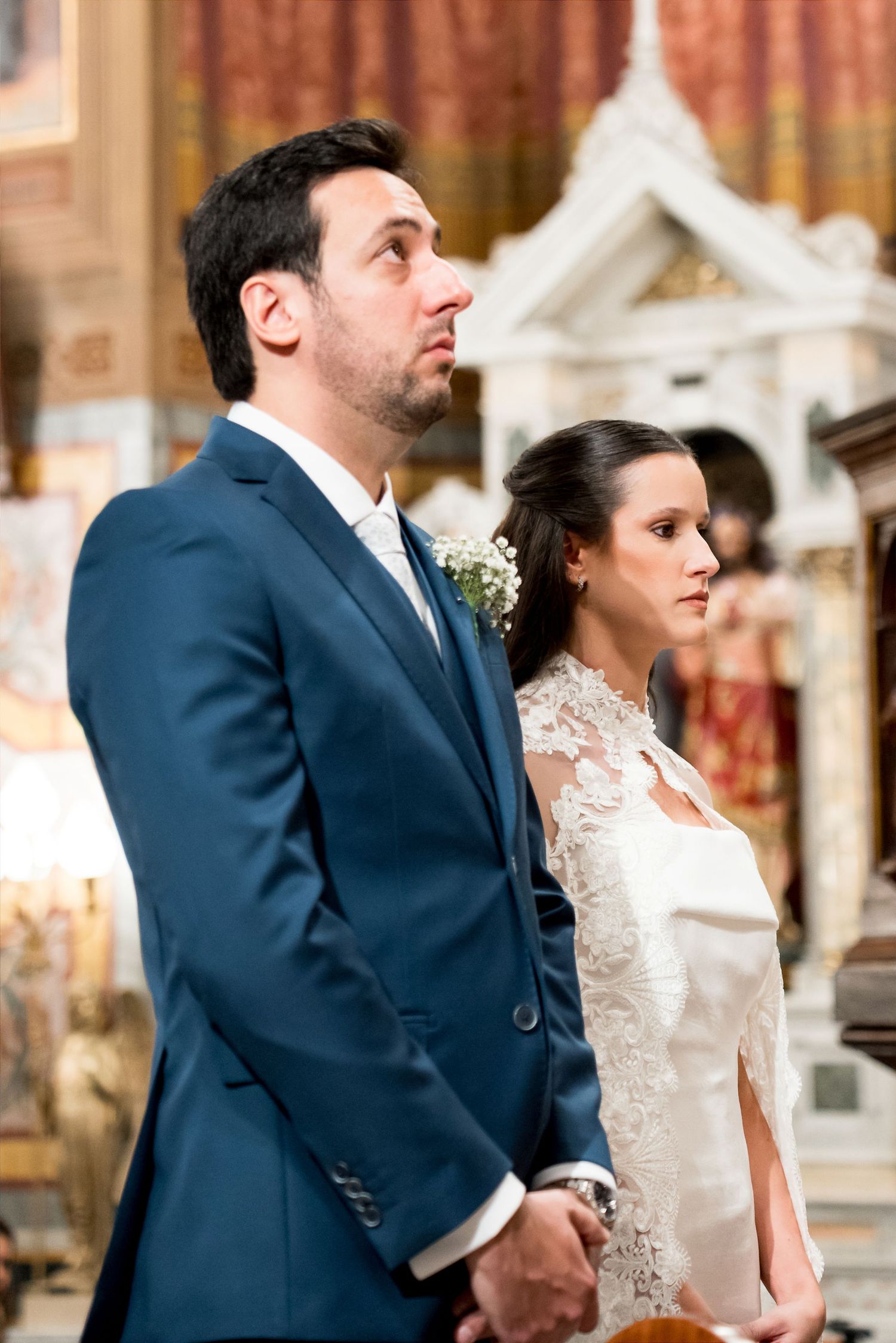 A bride and groom stand together during a church wedding ceremony, dressed in elegant attire.