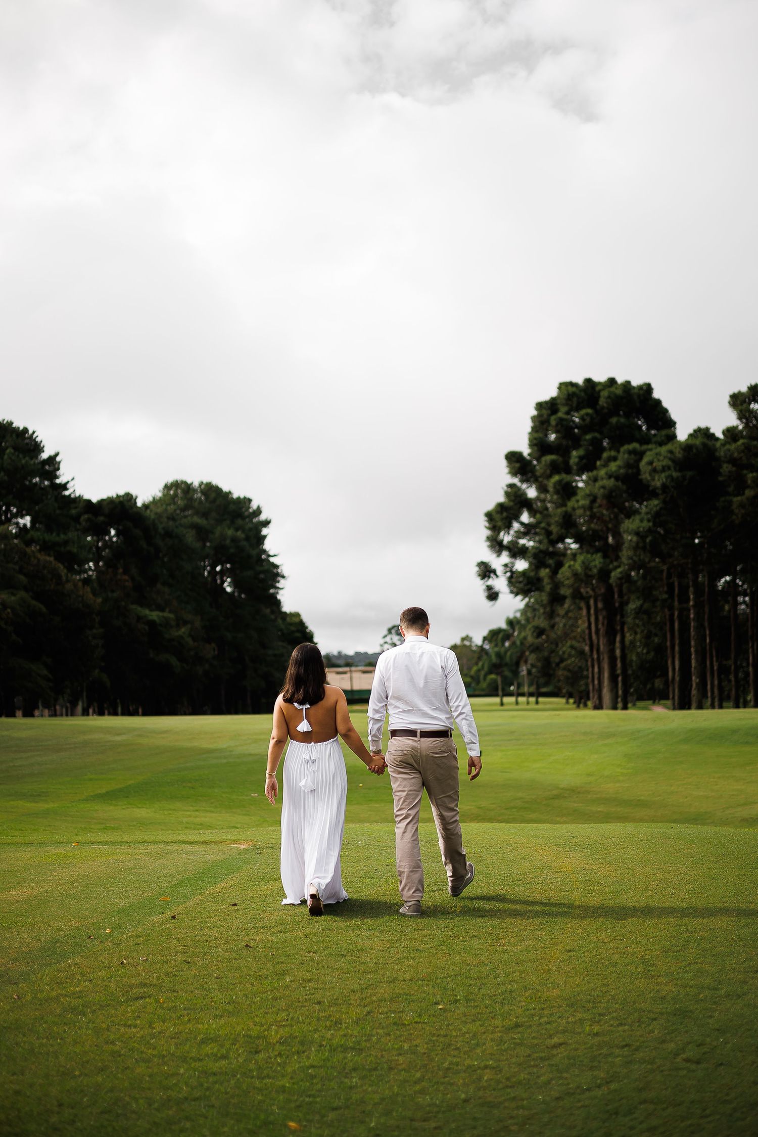 A couple walks hand-in-hand across a lush green golf course, the bride in a white dress and groom in khaki pants.