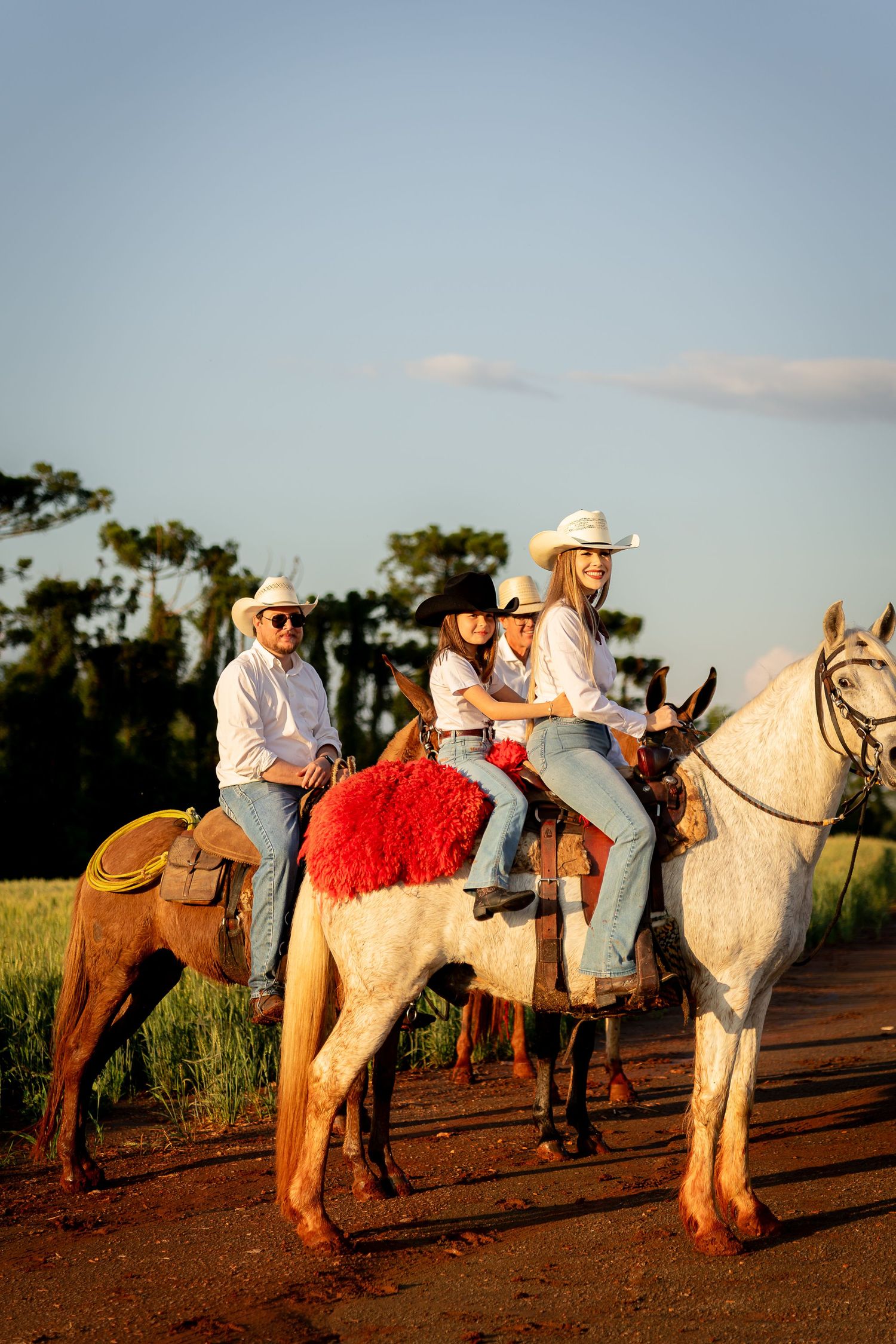 Family of four in cowboy hats riding horses on a rural dirt road at golden hour.