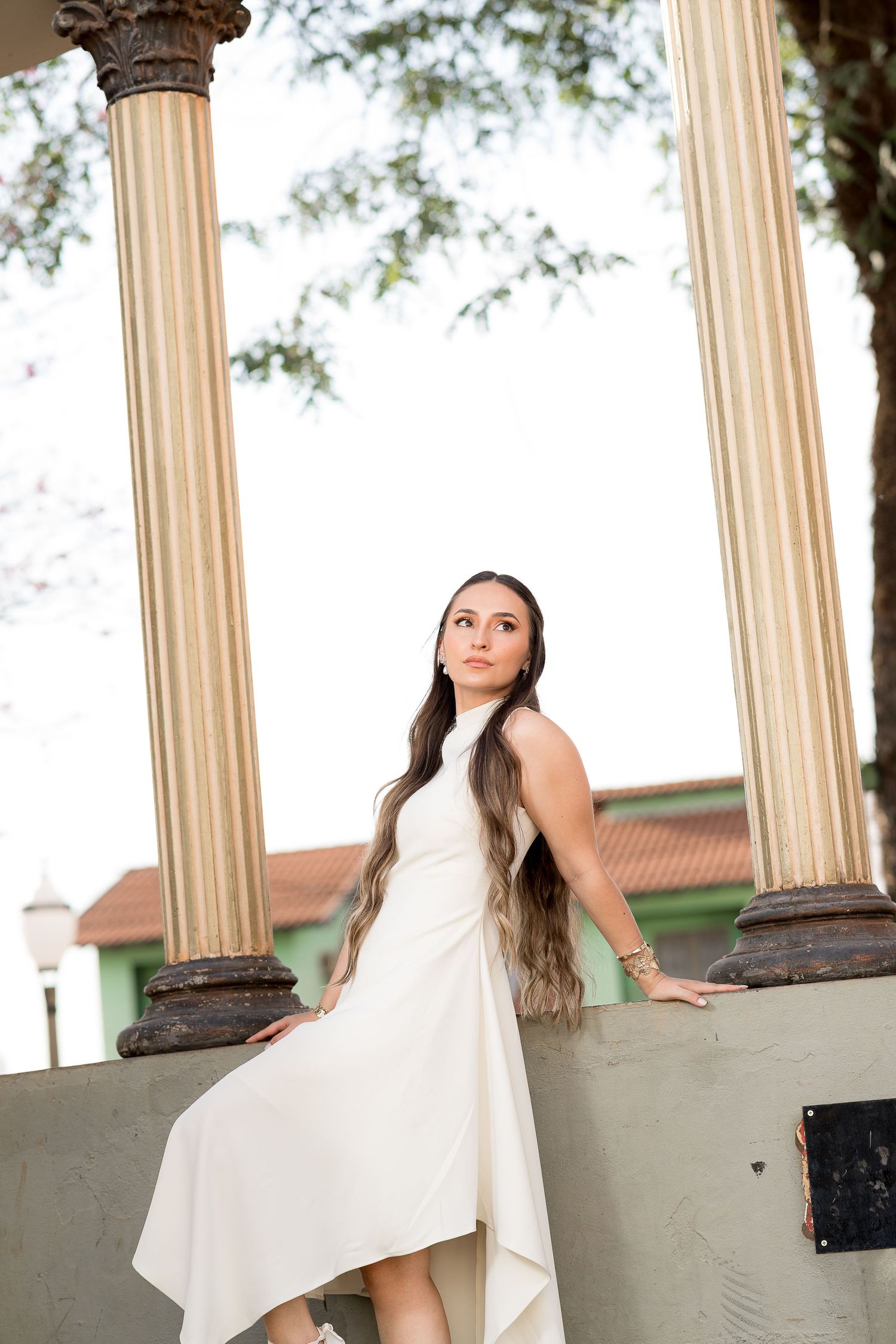 Young woman in elegant white dress posing gracefully between classical columns in an outdoor setting.