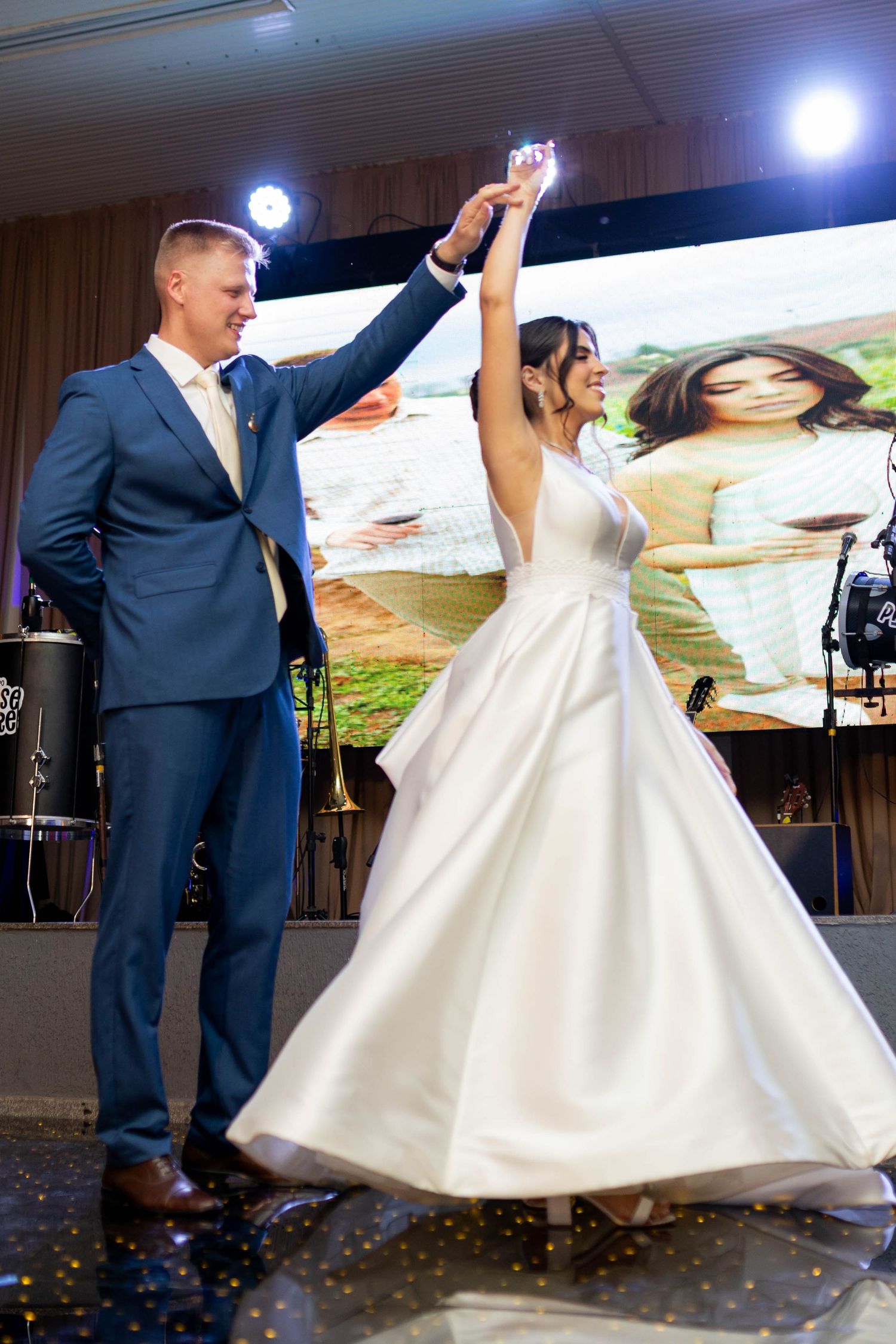 Bride and groom share first dance at wedding reception, bride in white gown twirling under groom's hand.