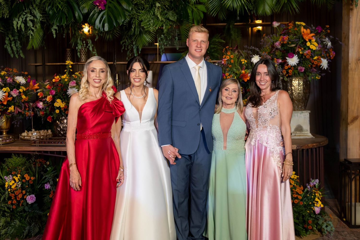 Five elegantly dressed guests pose together at a floral-decorated wedding reception venue.