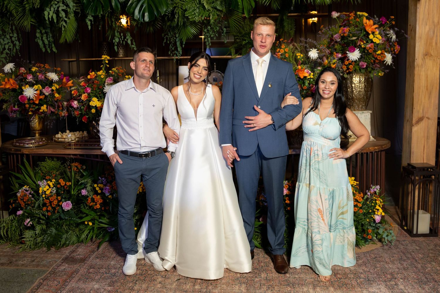 Two couples posing together at a wedding reception surrounded by lush floral arrangements.
