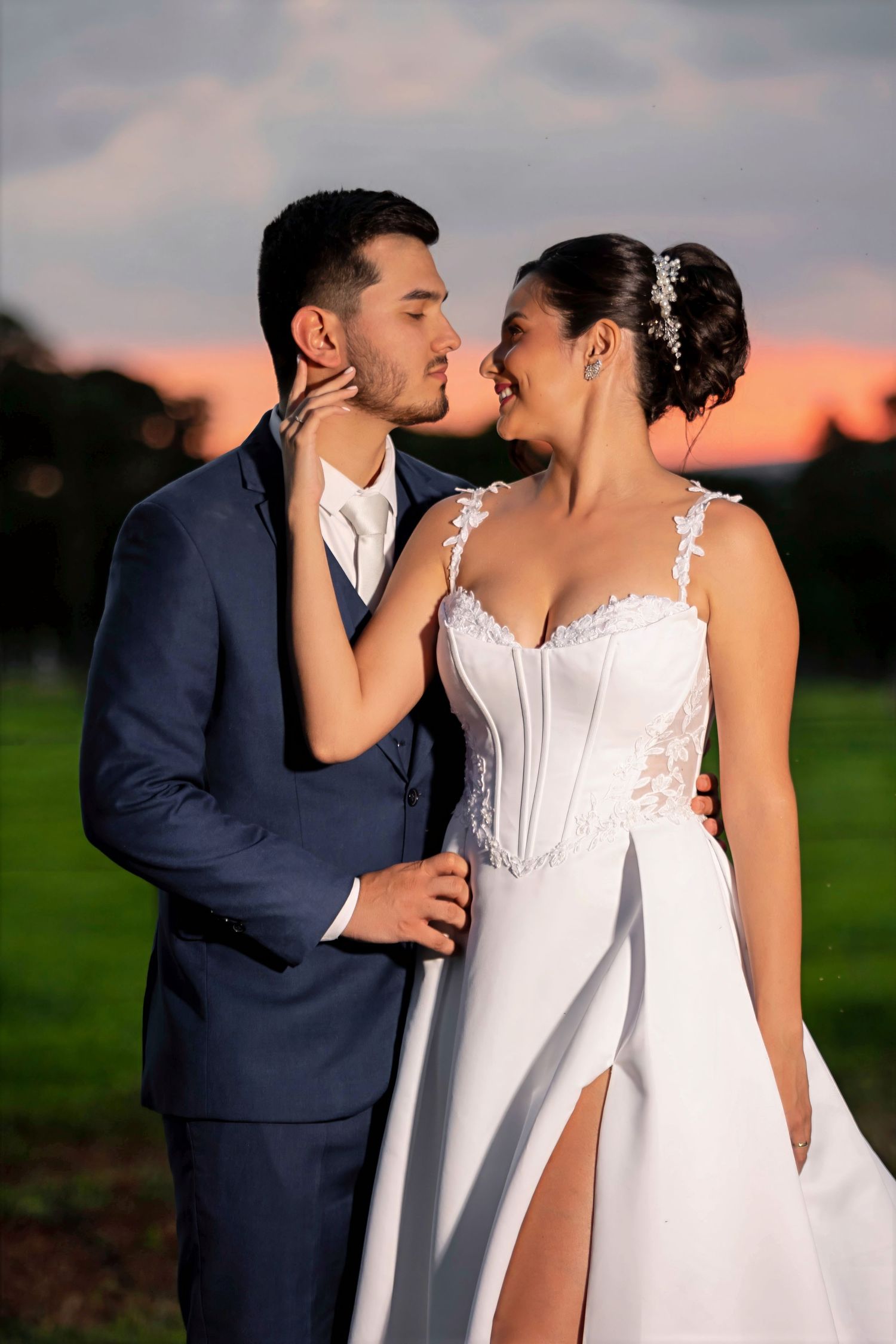 Bride and groom share a romantic kiss at sunset, she in a white lace gown, he in a navy suit.