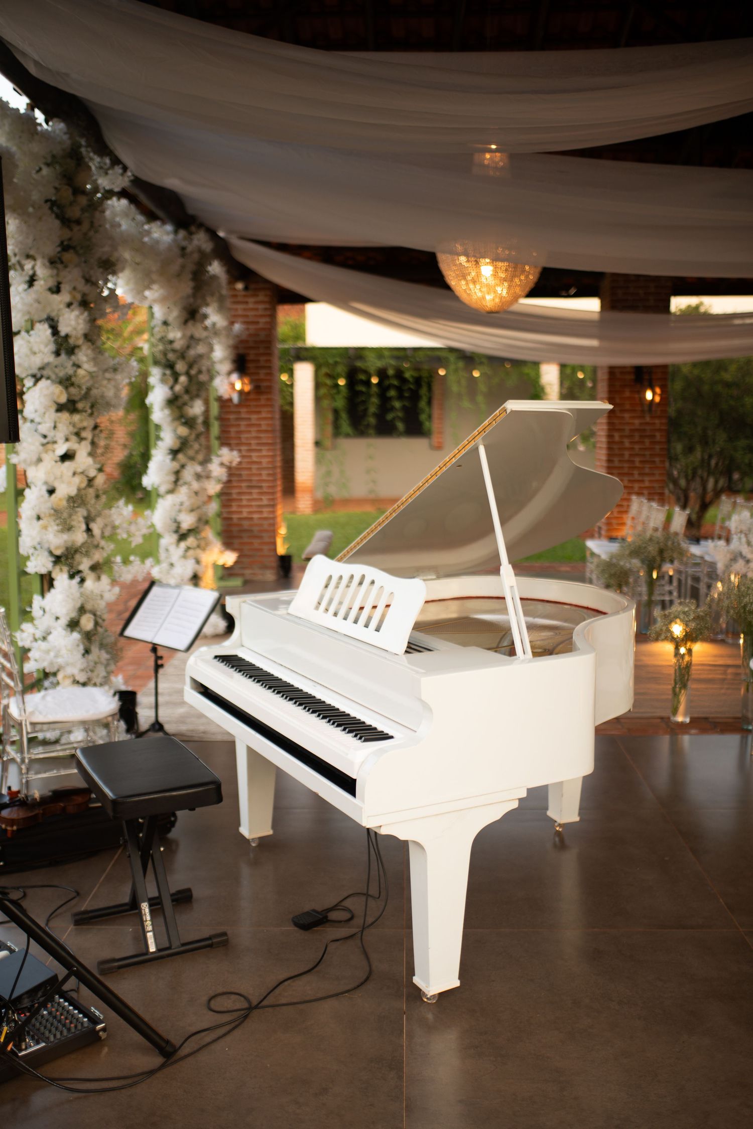 White grand piano with open lid on a tiled floor at an elegant outdoor wedding venue with floral decor.