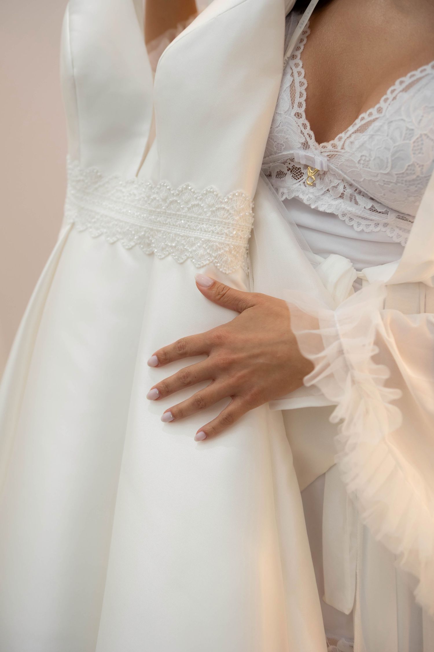 Bride in white lace lingerie holding a elegant satin wedding dress with delicate lace waistband detail.