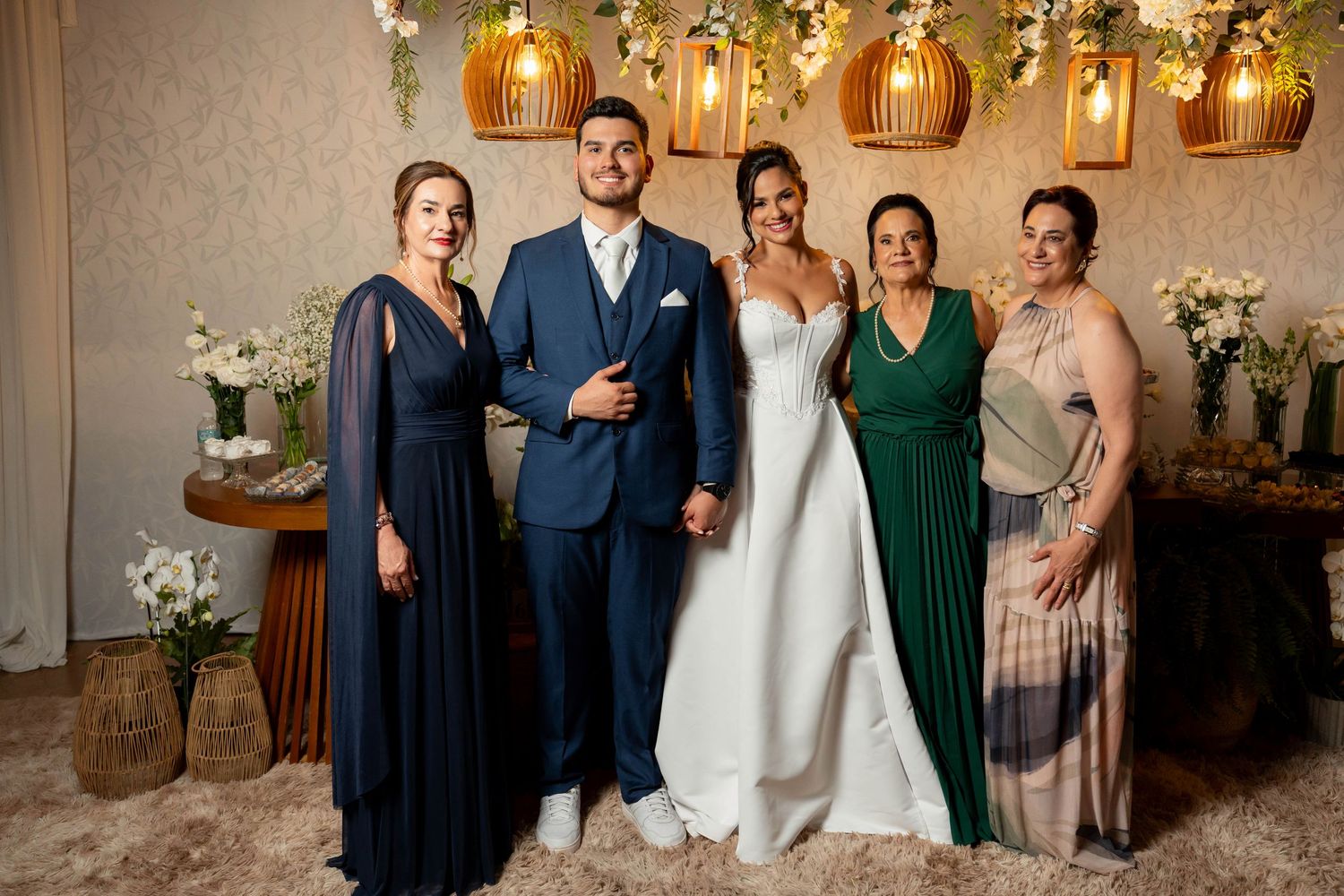 Wedding party of five poses together indoors with floral decorations and warm lighting.
