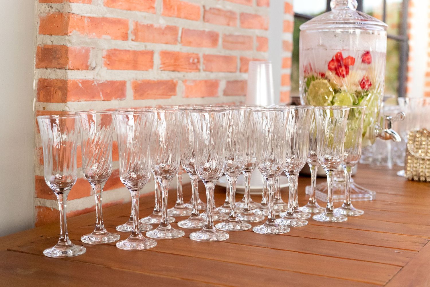 Elegant crystal wine and champagne glasses arranged on a wooden table near a brick wall at an event.