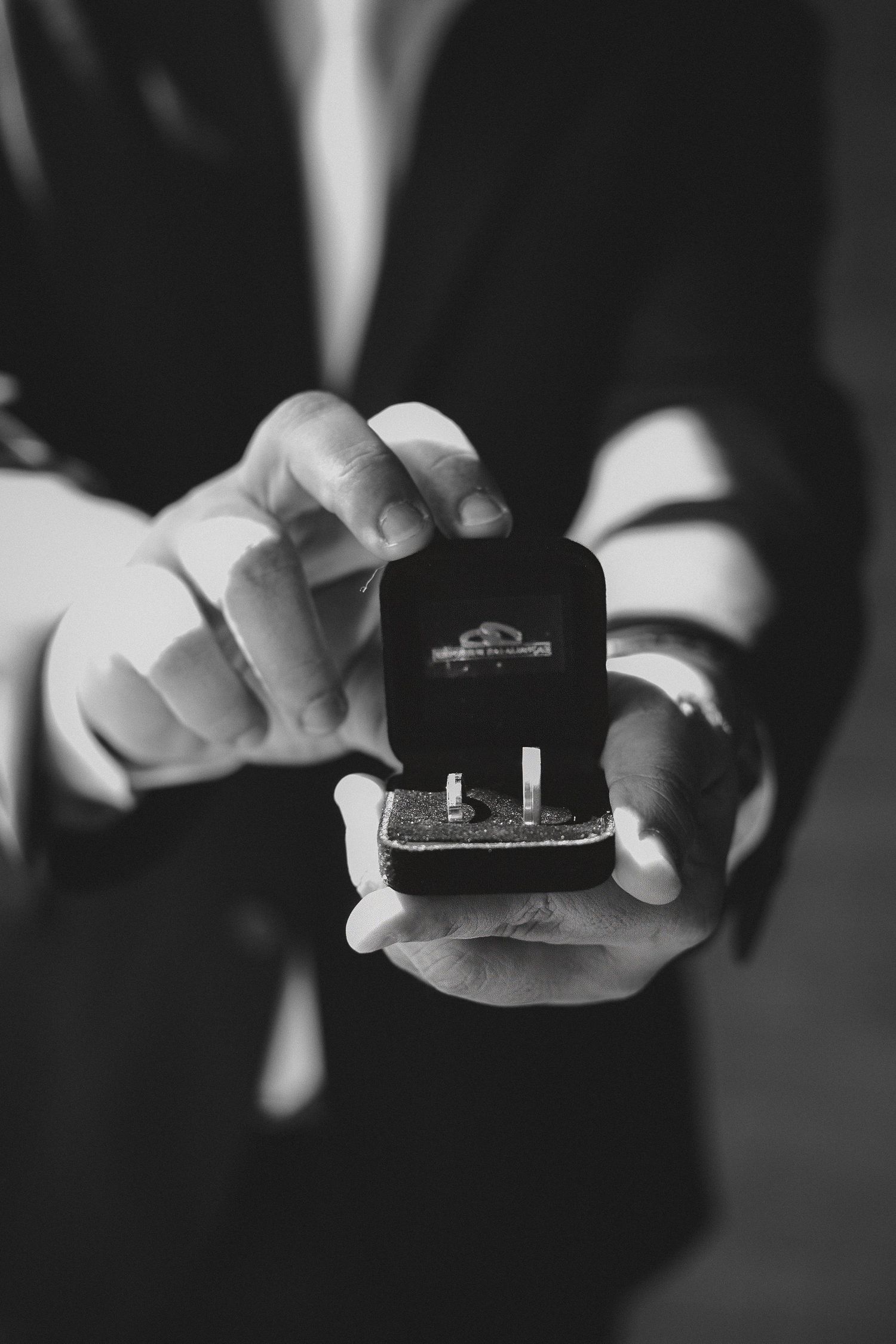 Black and white photo of hands holding an open ring box with two wedding bands inside.