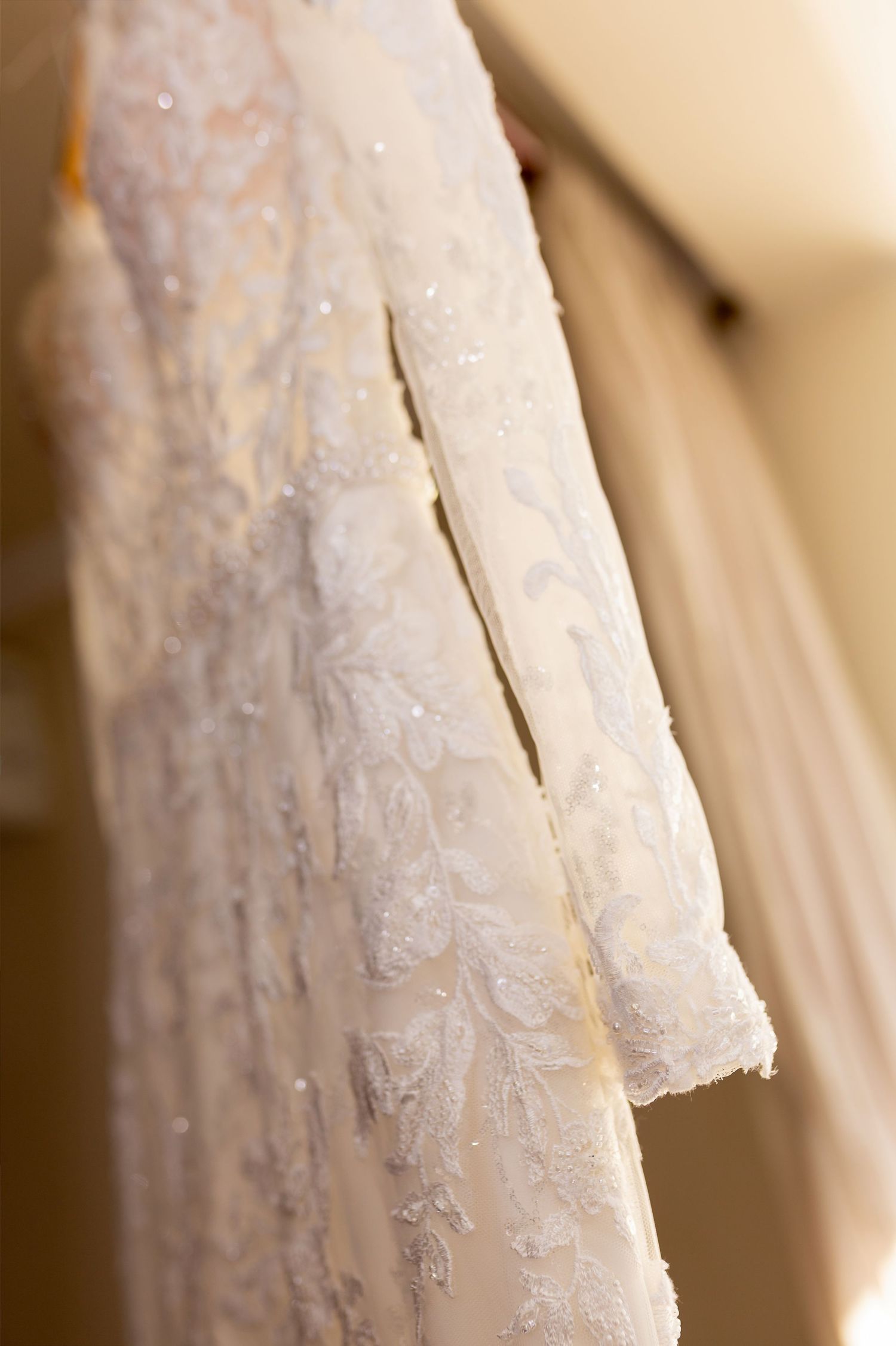 Close-up of an elegant white lace beaded wedding dress hanging, showcasing intricate floral embroidery details.