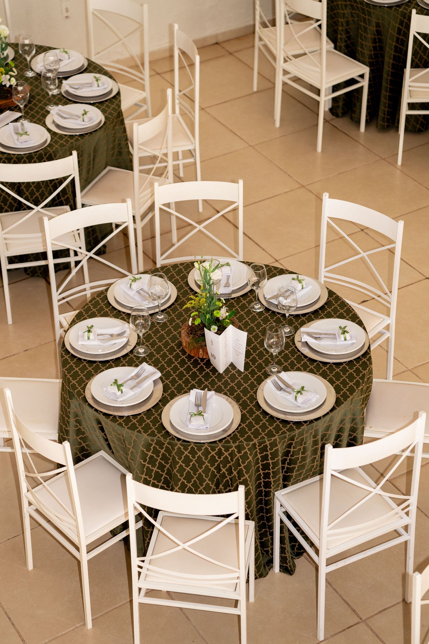 Elegant round tables with dark green patterned tablecloths, white chairs, and formal place settings in a banquet hall.
