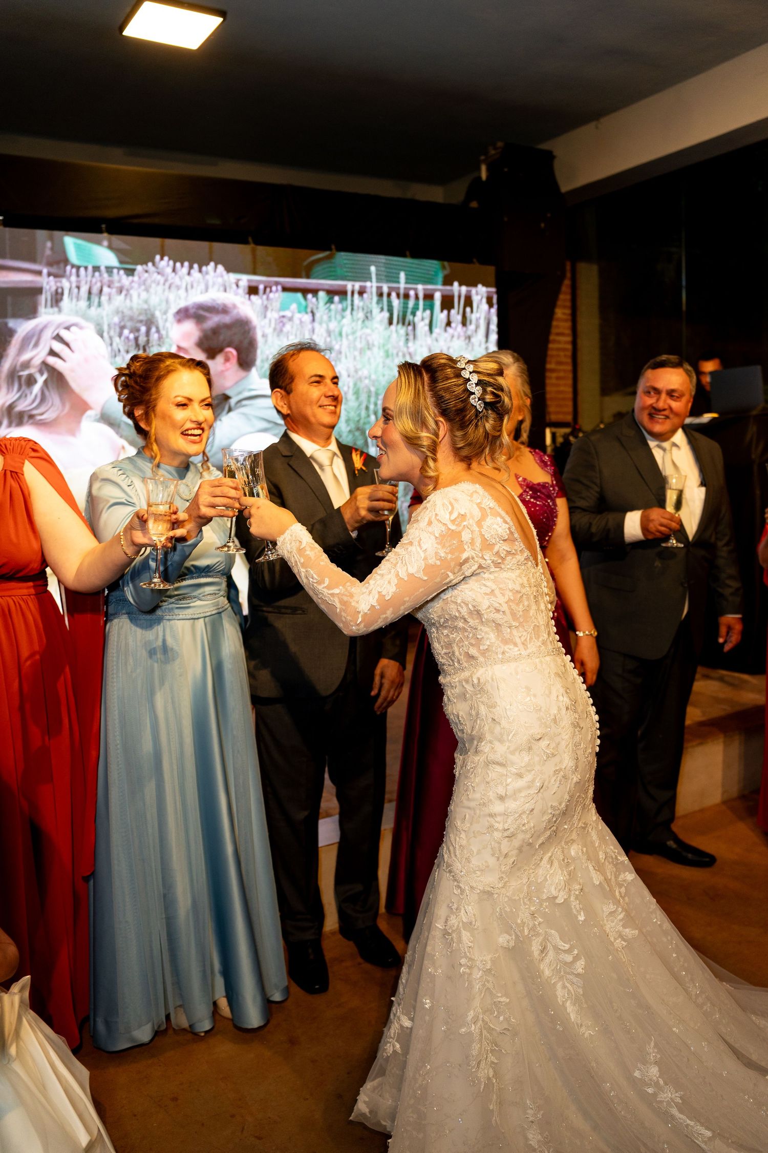 Bride in lace gown toasts with bridesmaids in blue and red dresses at elegant wedding reception.