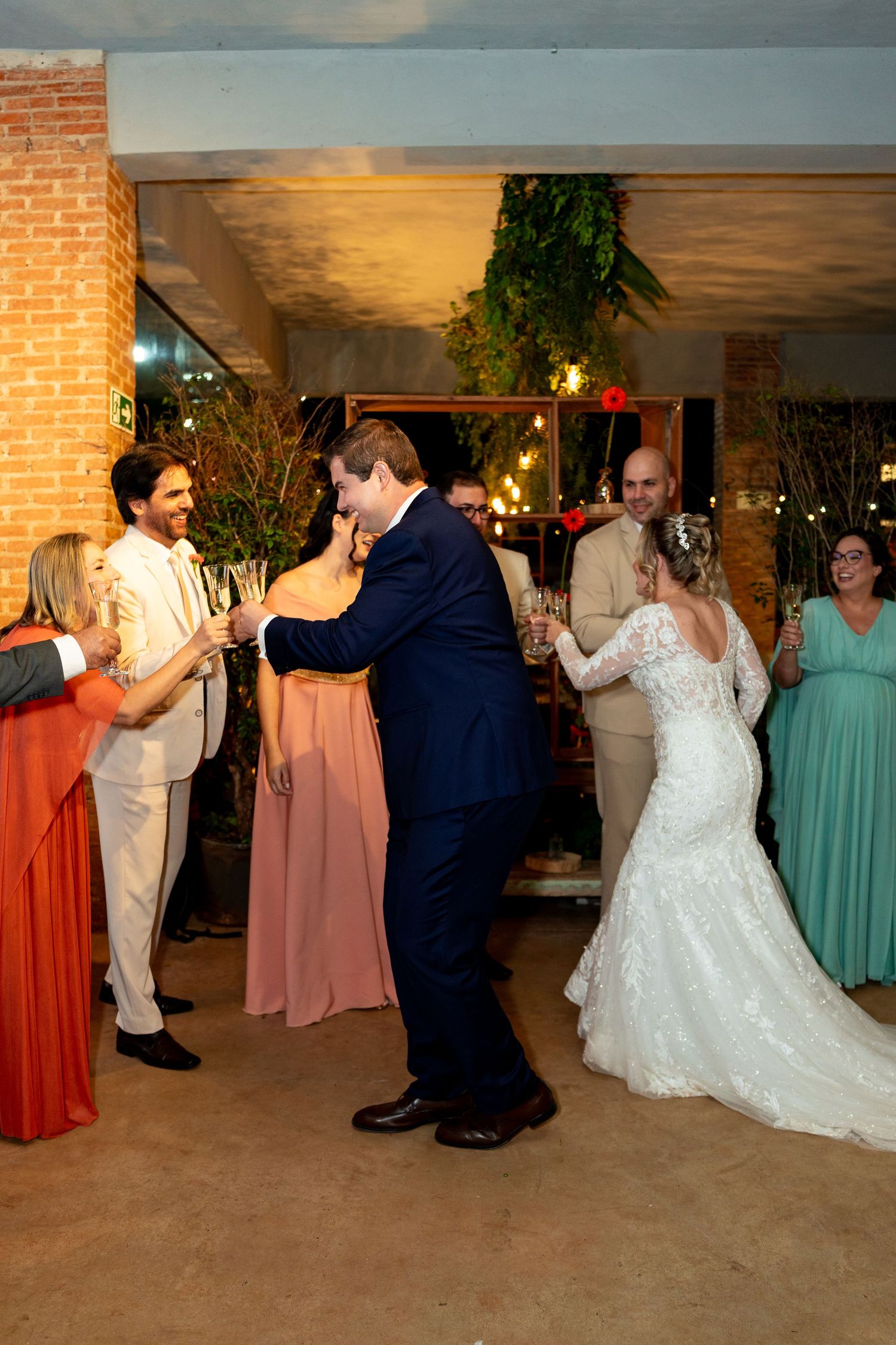 Bride in lace gown and groom in navy suit share first dance at elegant indoor wedding reception.