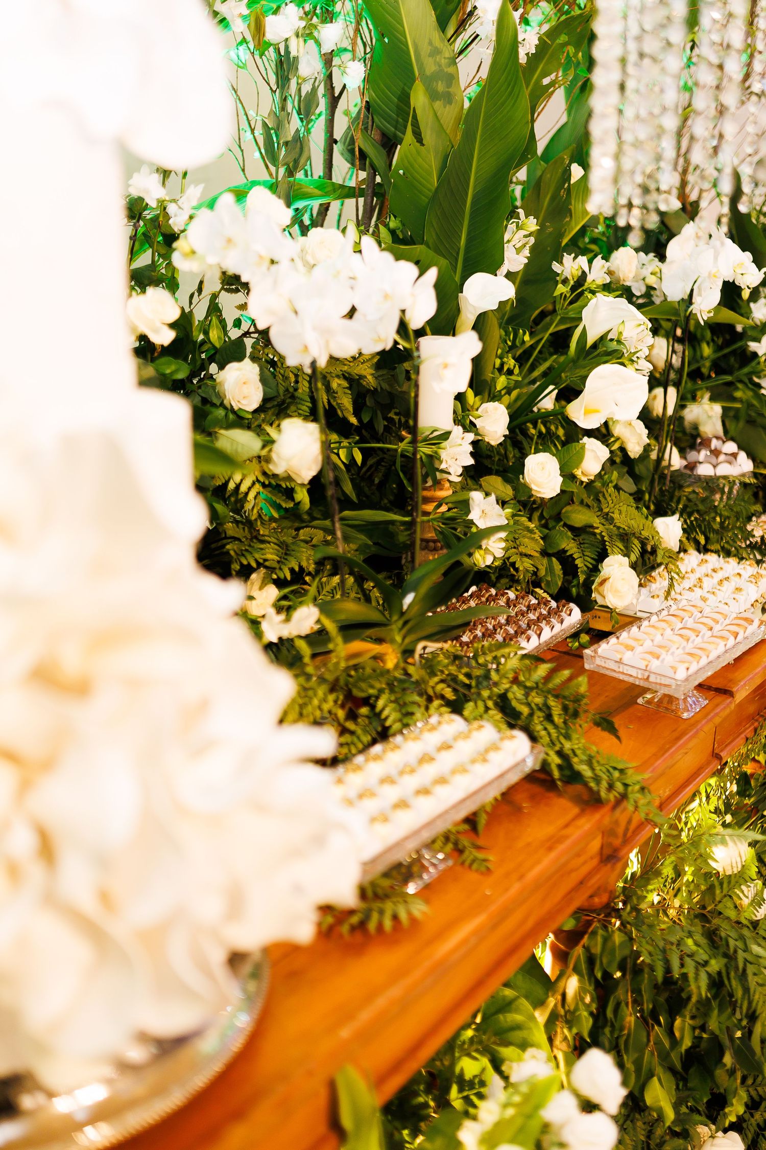 Elegant wedding dessert table with white orchids, lush greenery, and assorted sweets on a wooden table.