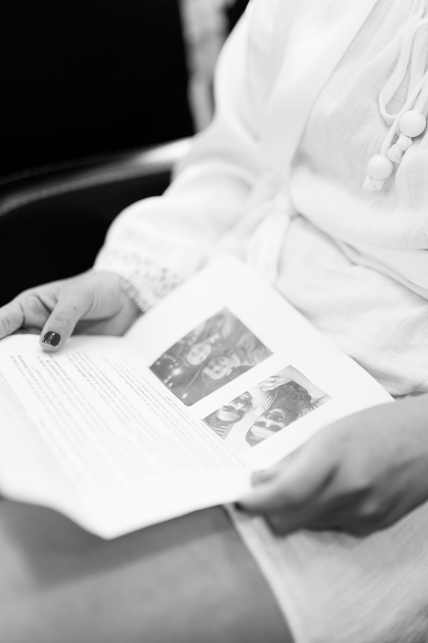 Black and white photo of a woman in a white robe holding a wedding program with photos during bridal preparations.