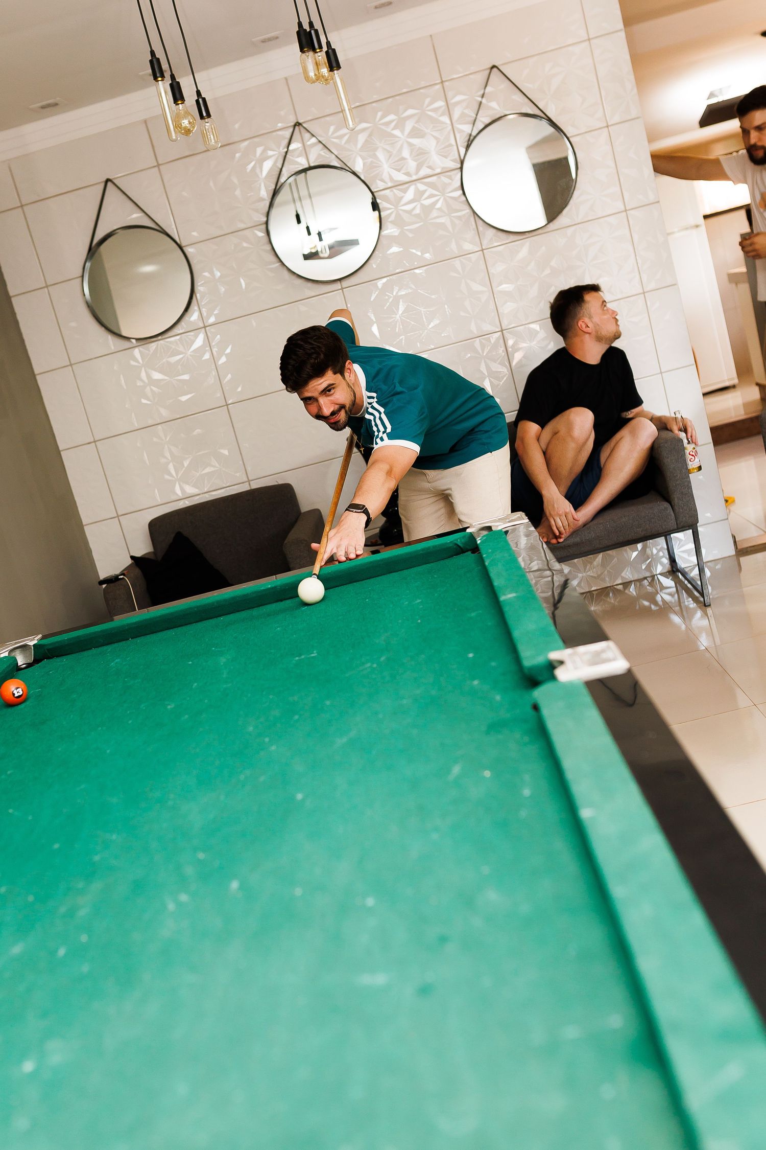 Two men enjoying a game of pool in a modern recreation room with round mirrors and pendant lights.